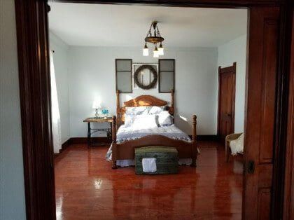 Spacious bedroom with polished wooden floor and bed framed by wooden doorway.