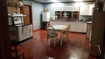 Vintage kitchen with red floor, white cabinets, and a wooden table. Old-fashioned stove and refrigerator present.