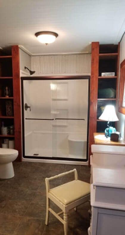 Bathroom with shower, built-in shelves, toilet, and vanity with a bench.
