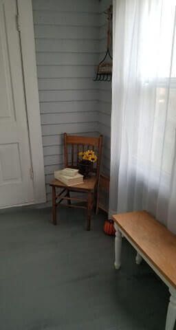 A small, wooden chair with flowers sits near a window and bench in a room with blue walls.