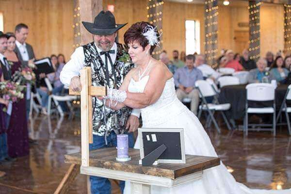 Couple lighting a unity candle during a wedding ceremony in a rustic barn, guests in the background.