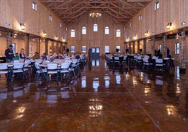 Large wood-paneled event space with tables, chairs, and guests; reflective floor; arched windows; chandeliers.