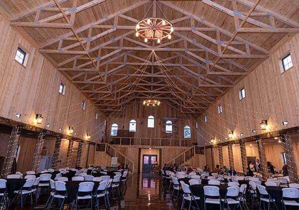 Large, wooden barn interior with tables and chairs set up for an event, chandelier.