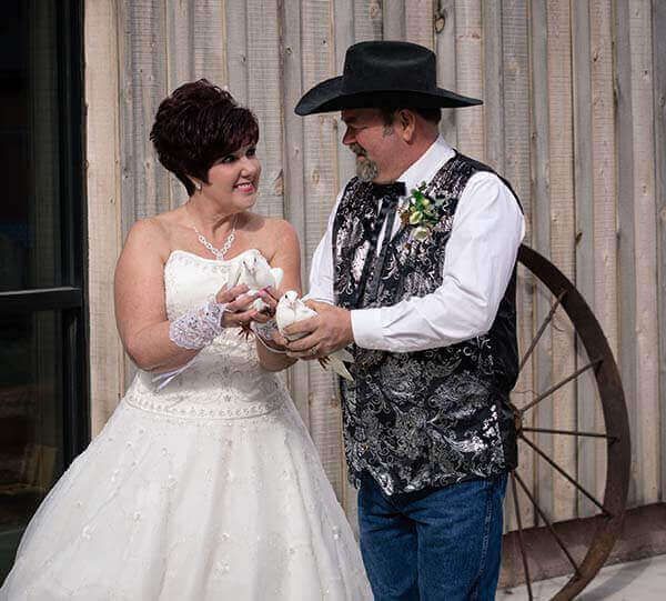 Bride and groom releasing doves at a wedding. Couple smiles, holding birds in front of a rustic wooden backdrop.