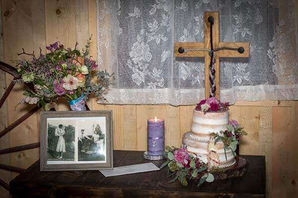 Wedding altar with cake, flowers, cross, photo, and candle on a wooden table.