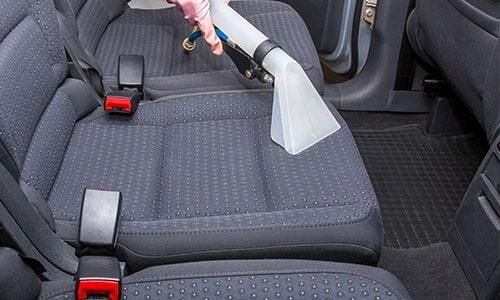 Una persona está limpiando los asientos de un coche con una aspiradora.