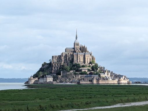 Mont Saint-Michel abbey on a rocky island surrounded by tidal flats and a calm, cloudy sky.