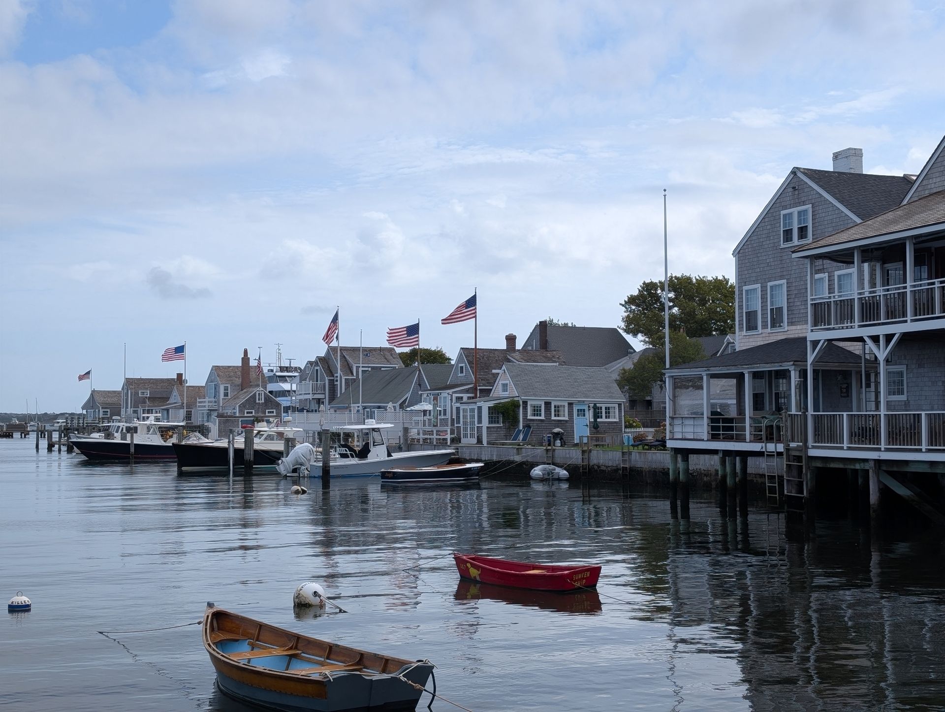 A harbor view of weathered waterfront houses with American flags, featuring small boats floating in calm water.