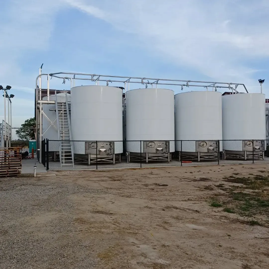 A row of white tanks are lined up in a dirt field.