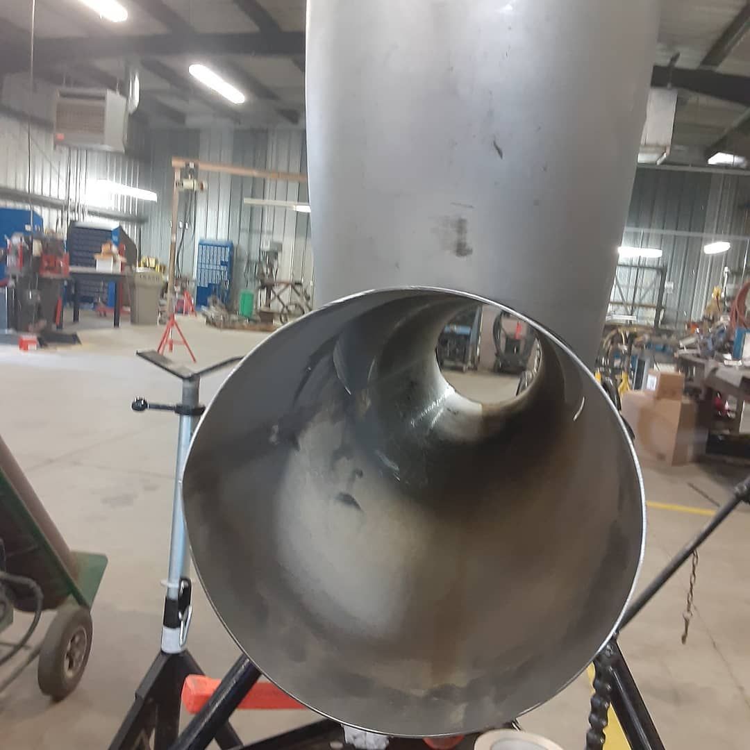 A stainless steel pipe is sitting on a stand in a factory