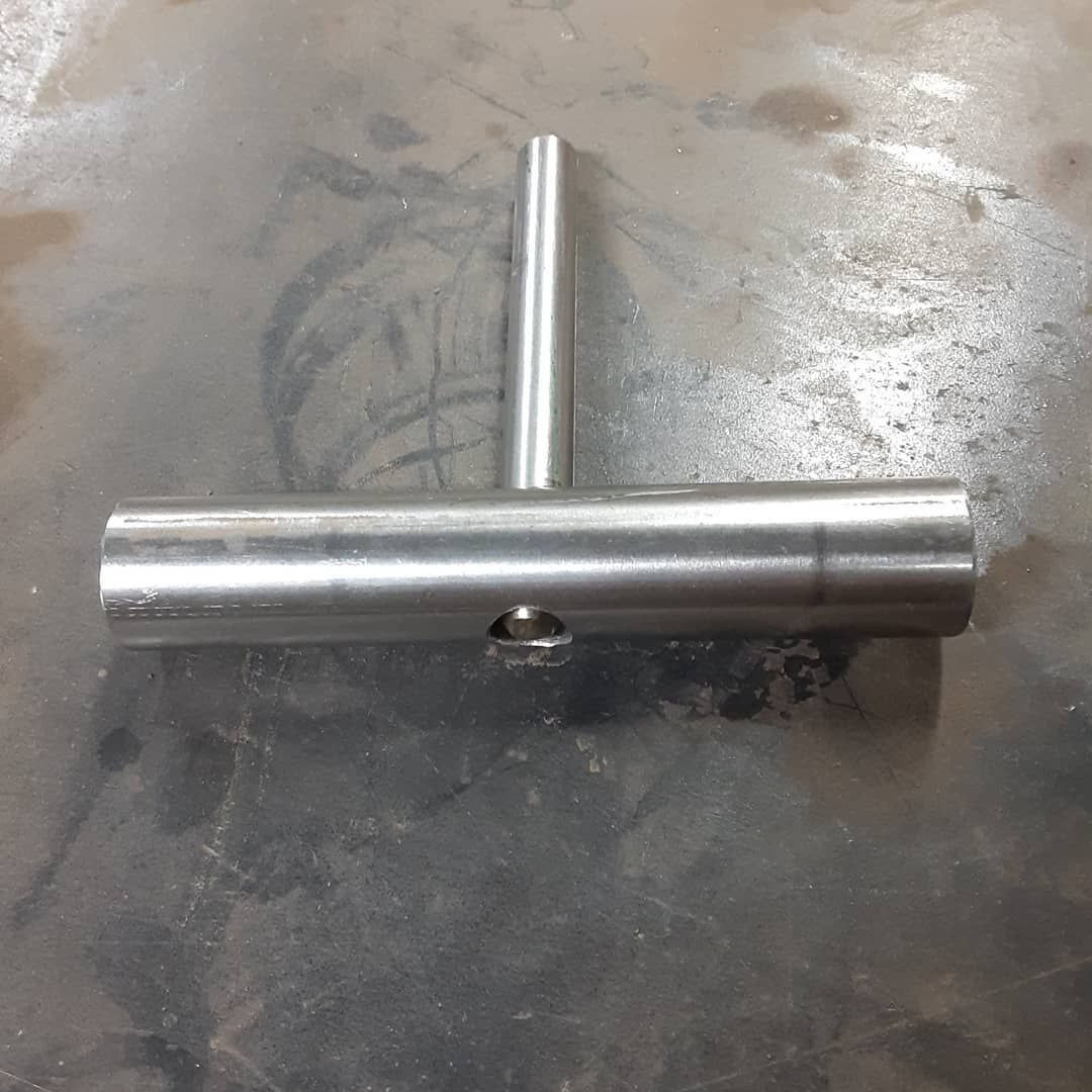 A stainless steel pipe with a hole in the middle is sitting on a metal surface.
