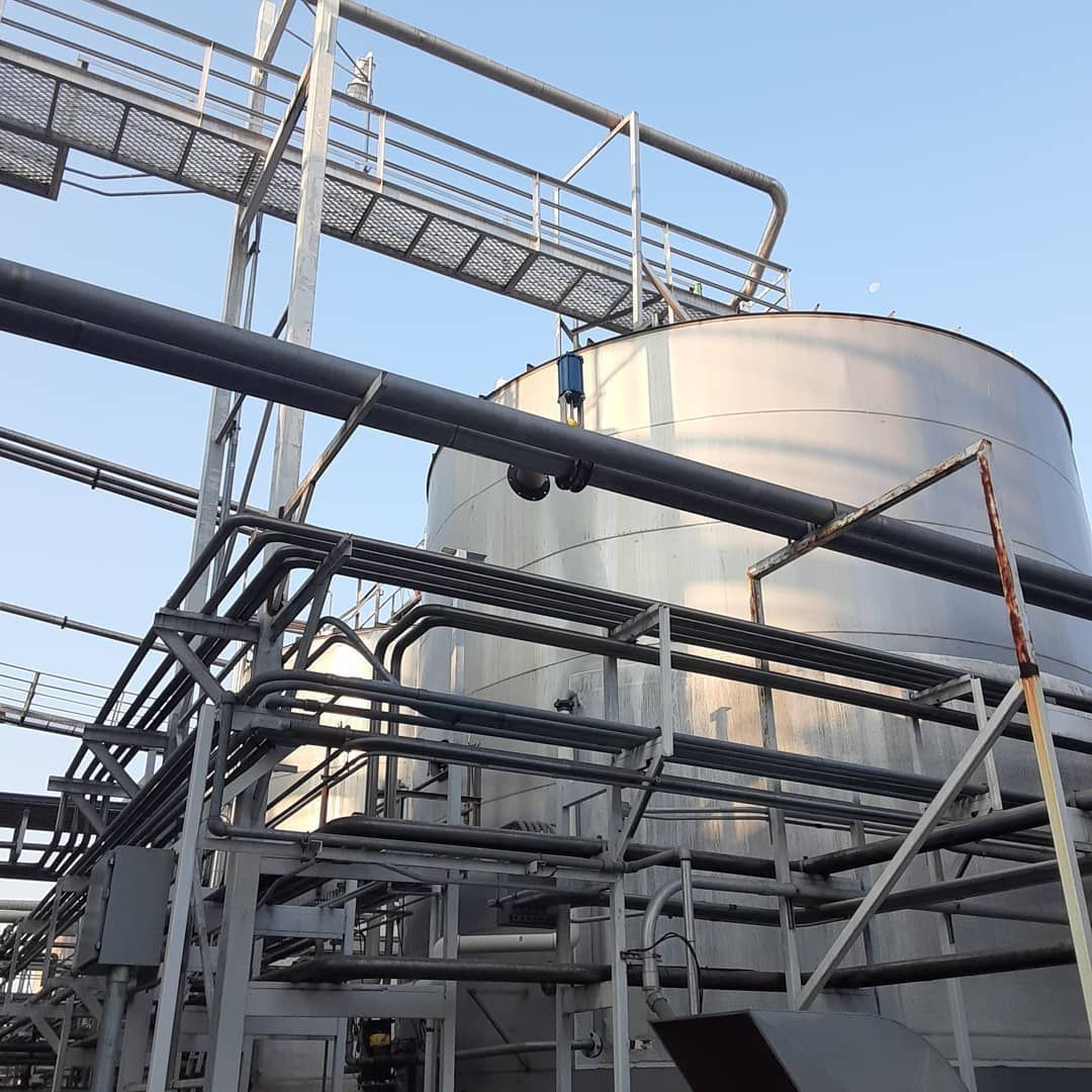 A large stainless steel tank is surrounded by pipes and stairs