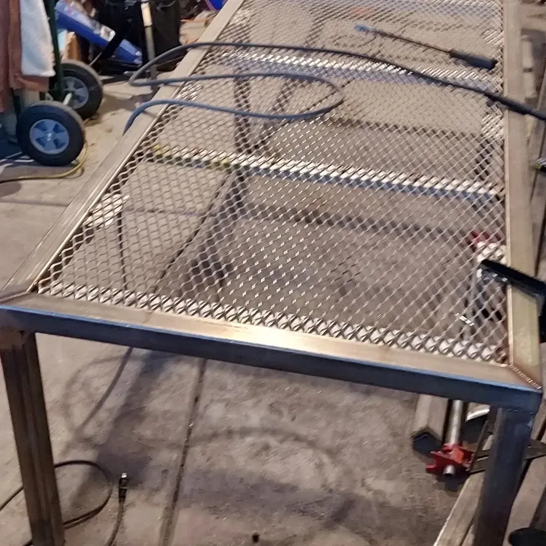 A metal table with a mesh top is being built in a garage.