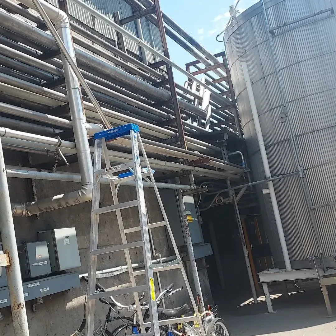 A ladder is sitting in front of a building with pipes.