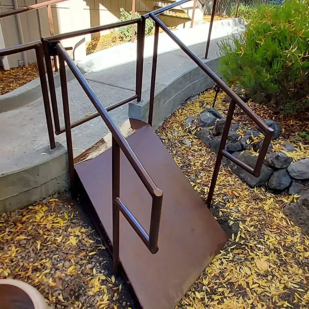 A staircase with a railing is surrounded by leaves and rocks.