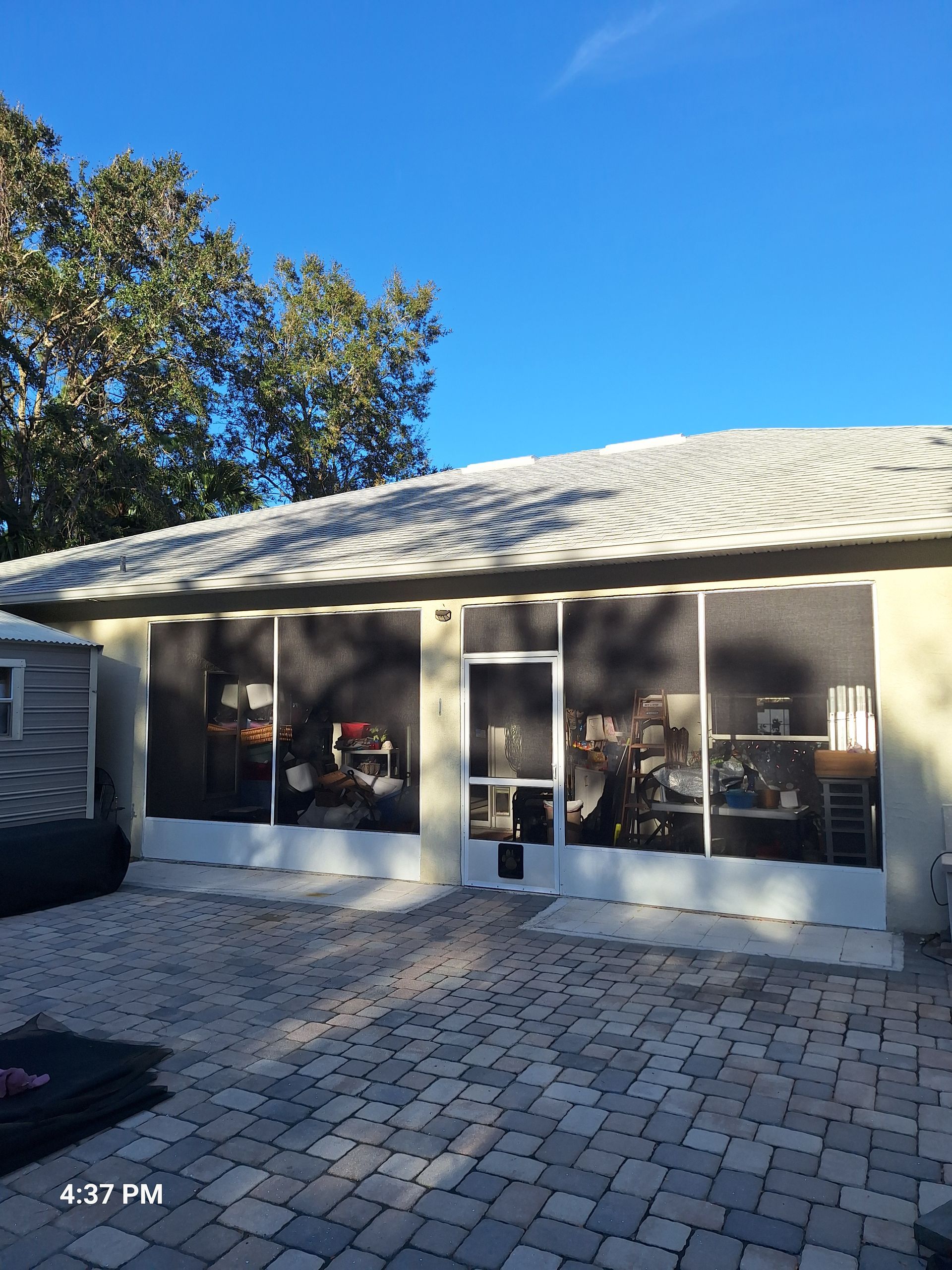 Screened-in patio with white trim, dark screens, and a brick-paved patio in bright sunlight.