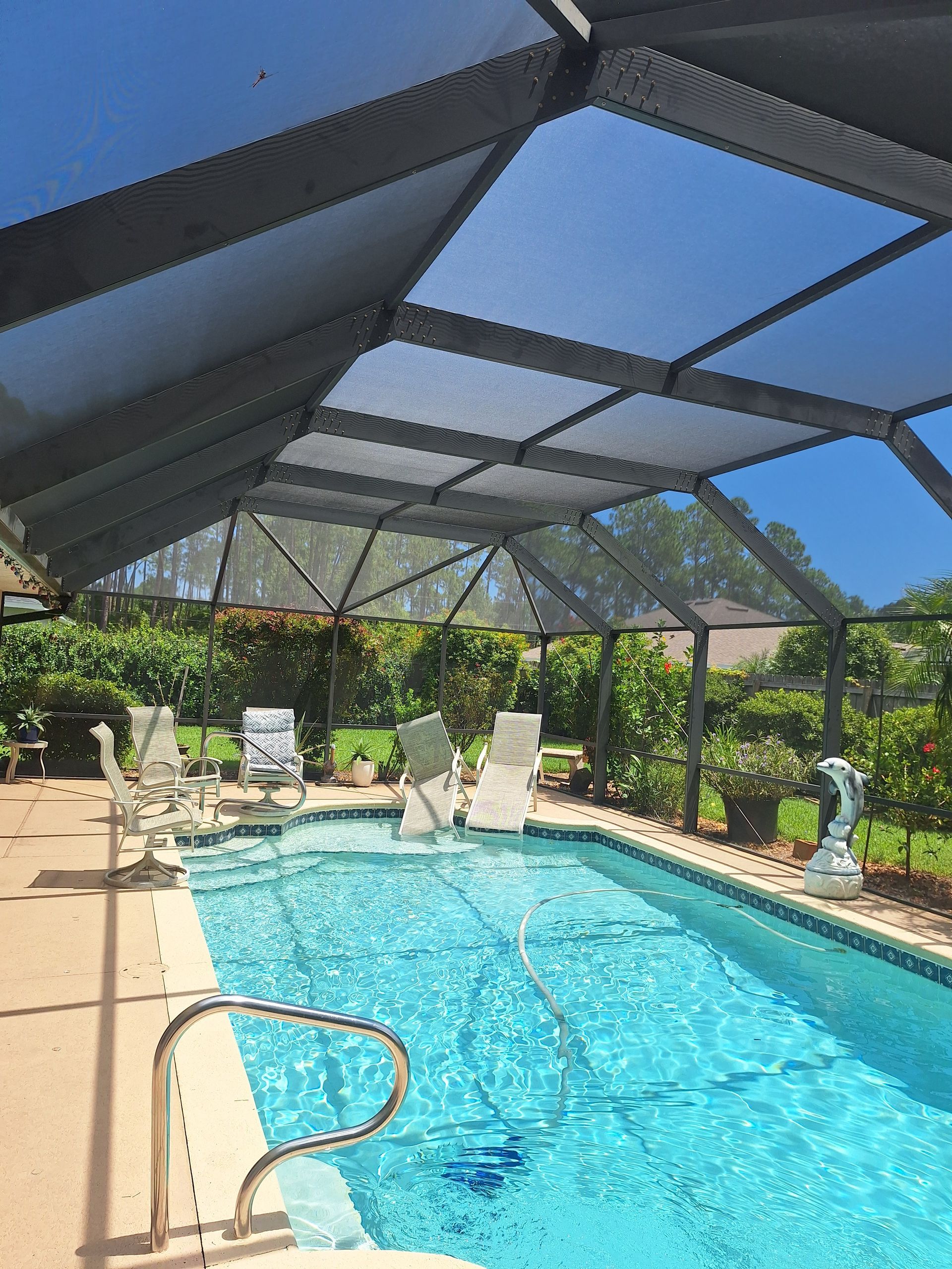 Pool enclosed by a screened lanai; blue water and sky, with lounge chairs and green foliage.