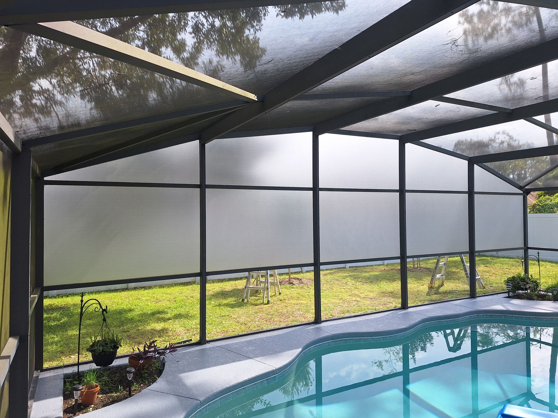 Screened-in pool enclosure with frosted panels, green lawn, and swimming pool.