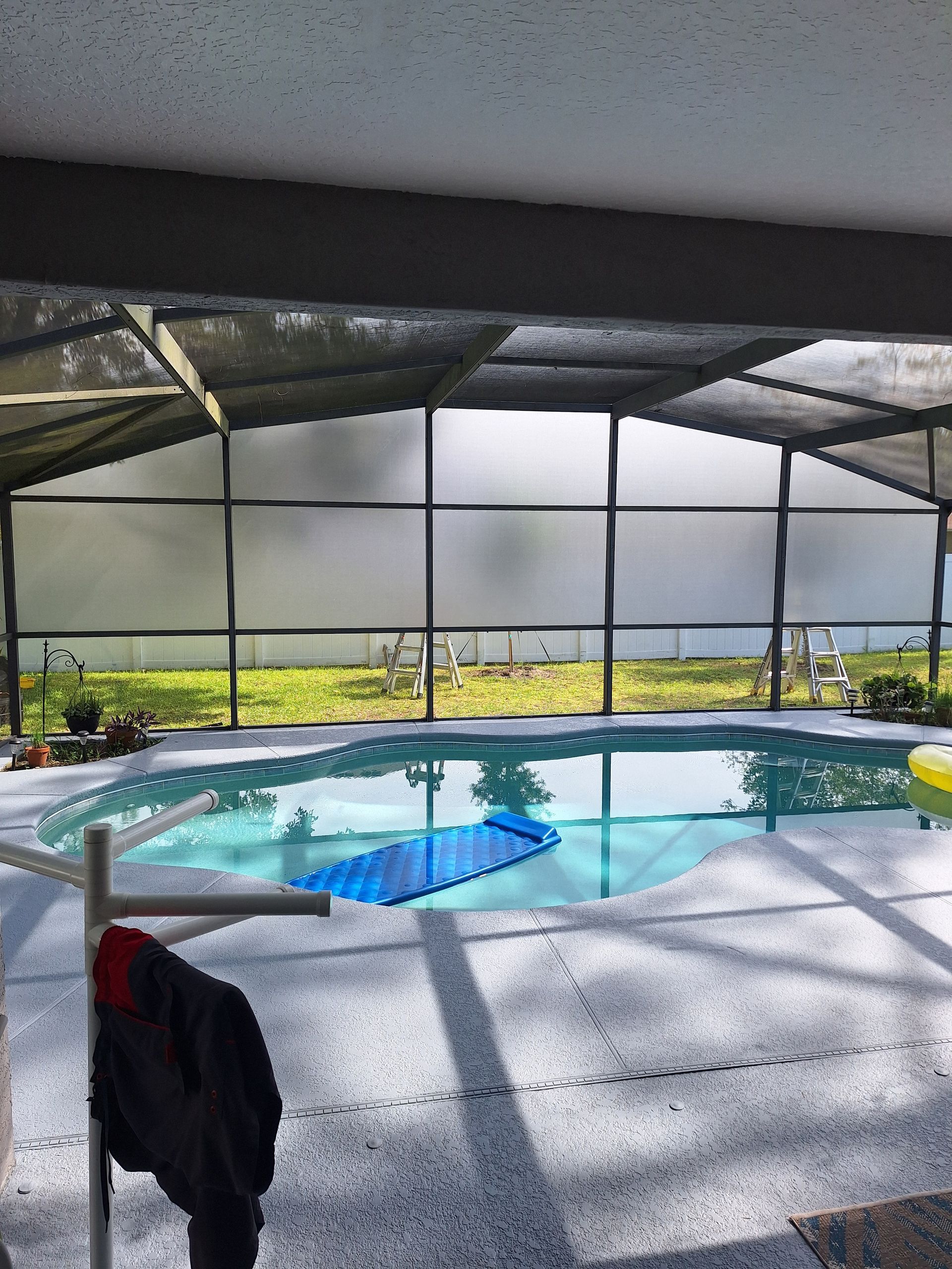 A screened-in pool with a blue pool cover, a black jacket hangs on a rack.