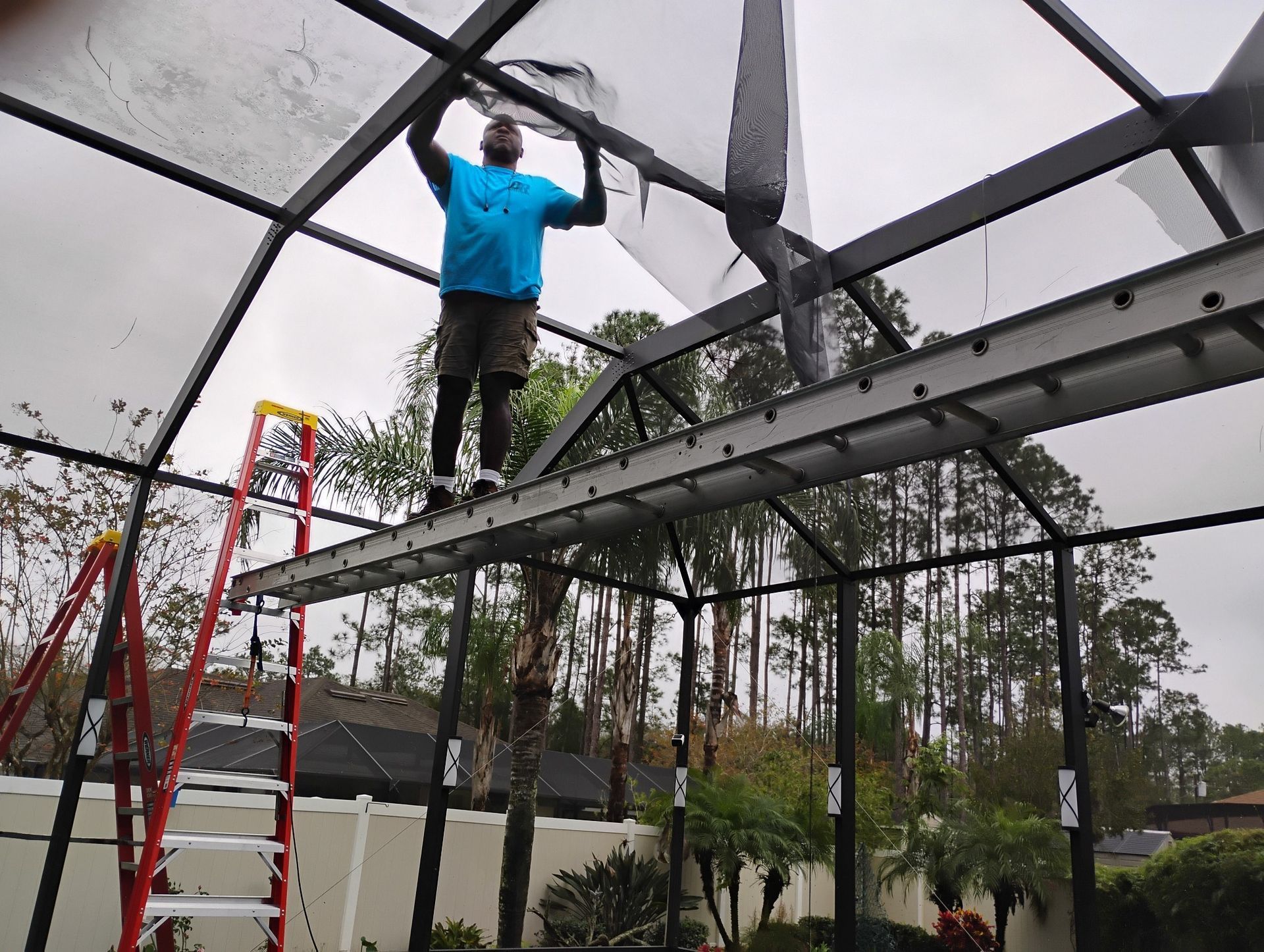 Man on ladder repairing a screened pool enclosure.