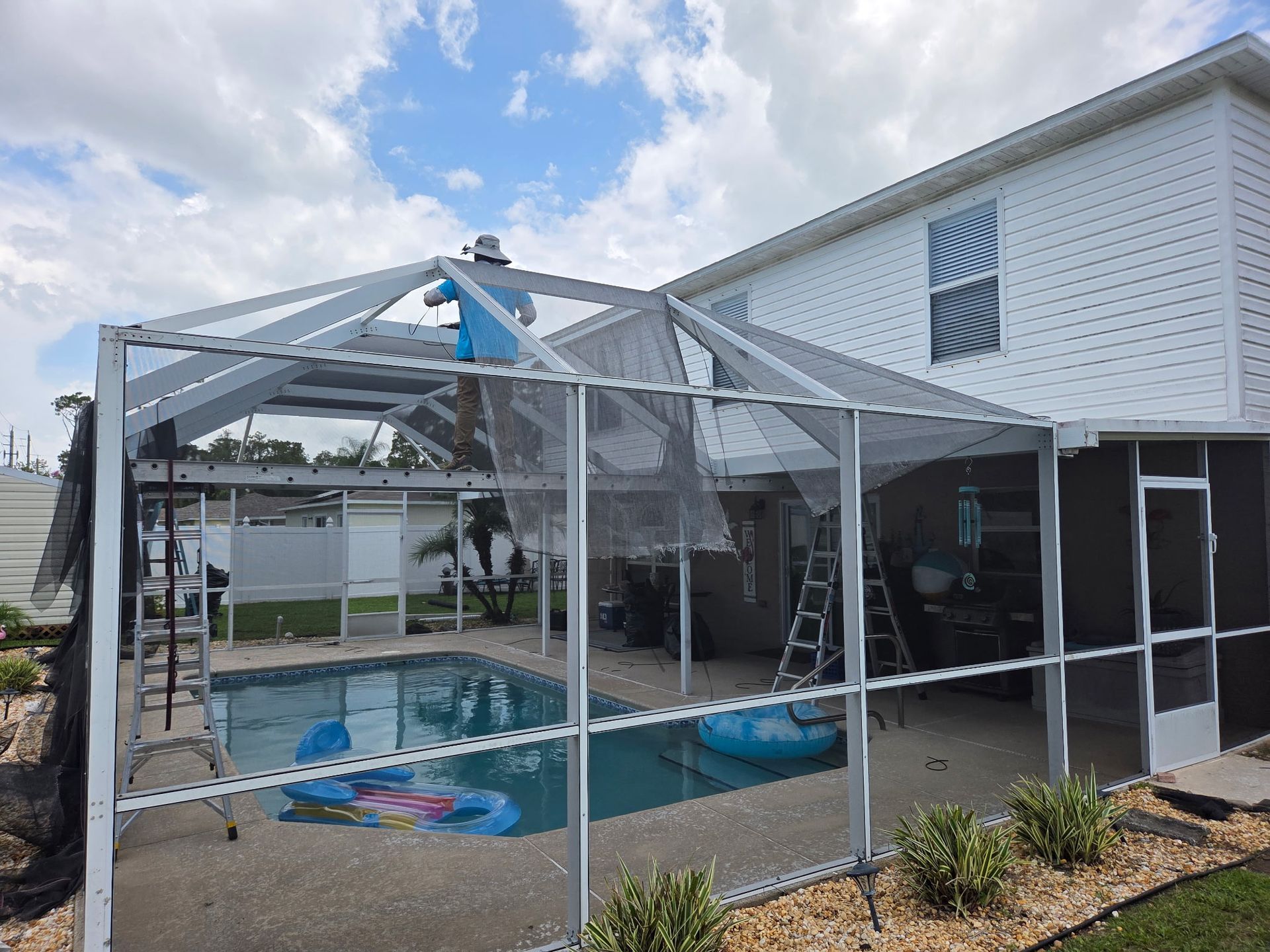 Pool enclosure with screen walls and roof, attached to a white house, blue pool and sky.