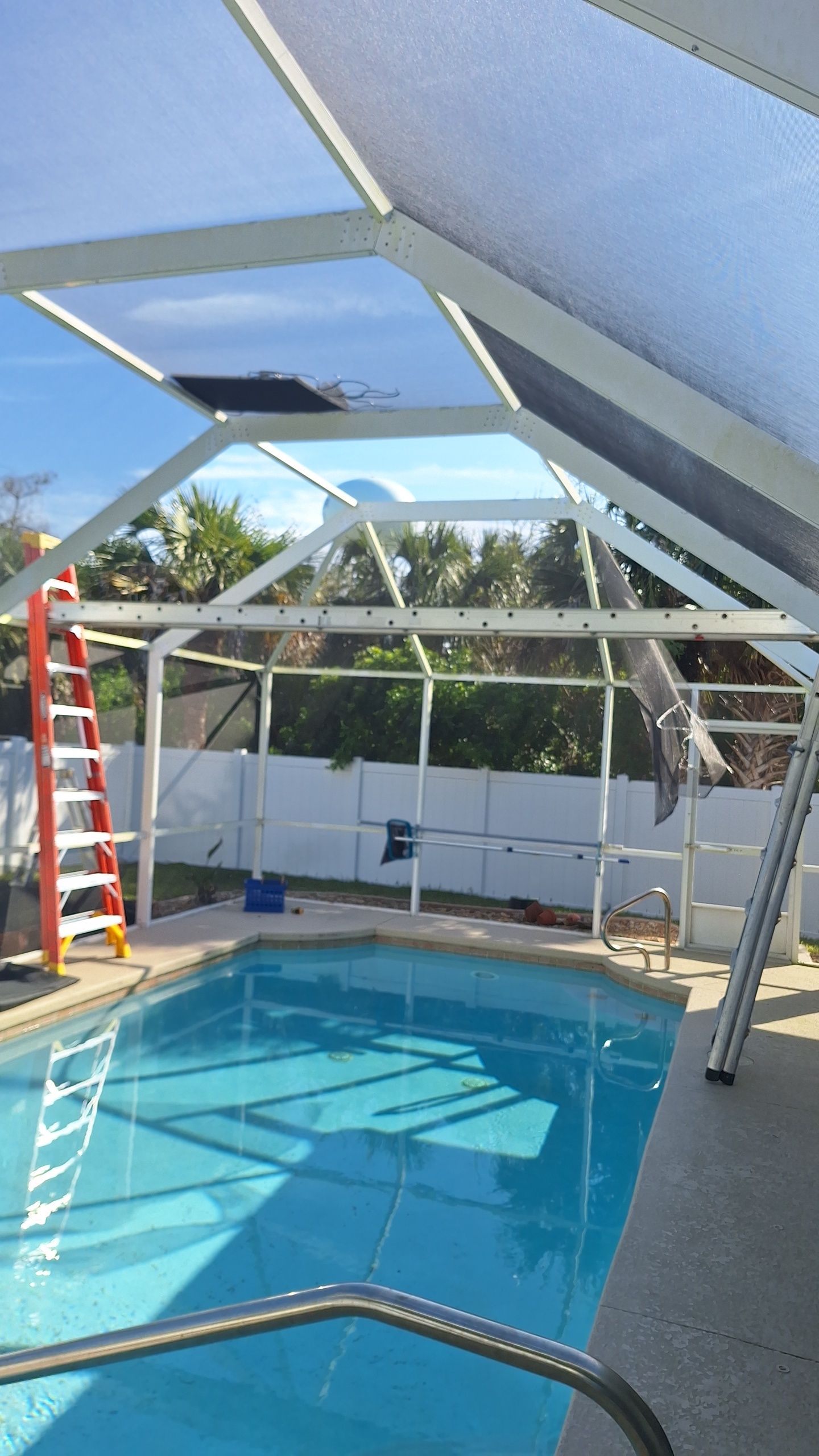 Pool with a damaged screen enclosure; ladder leaning against it. Blue water reflects sky.