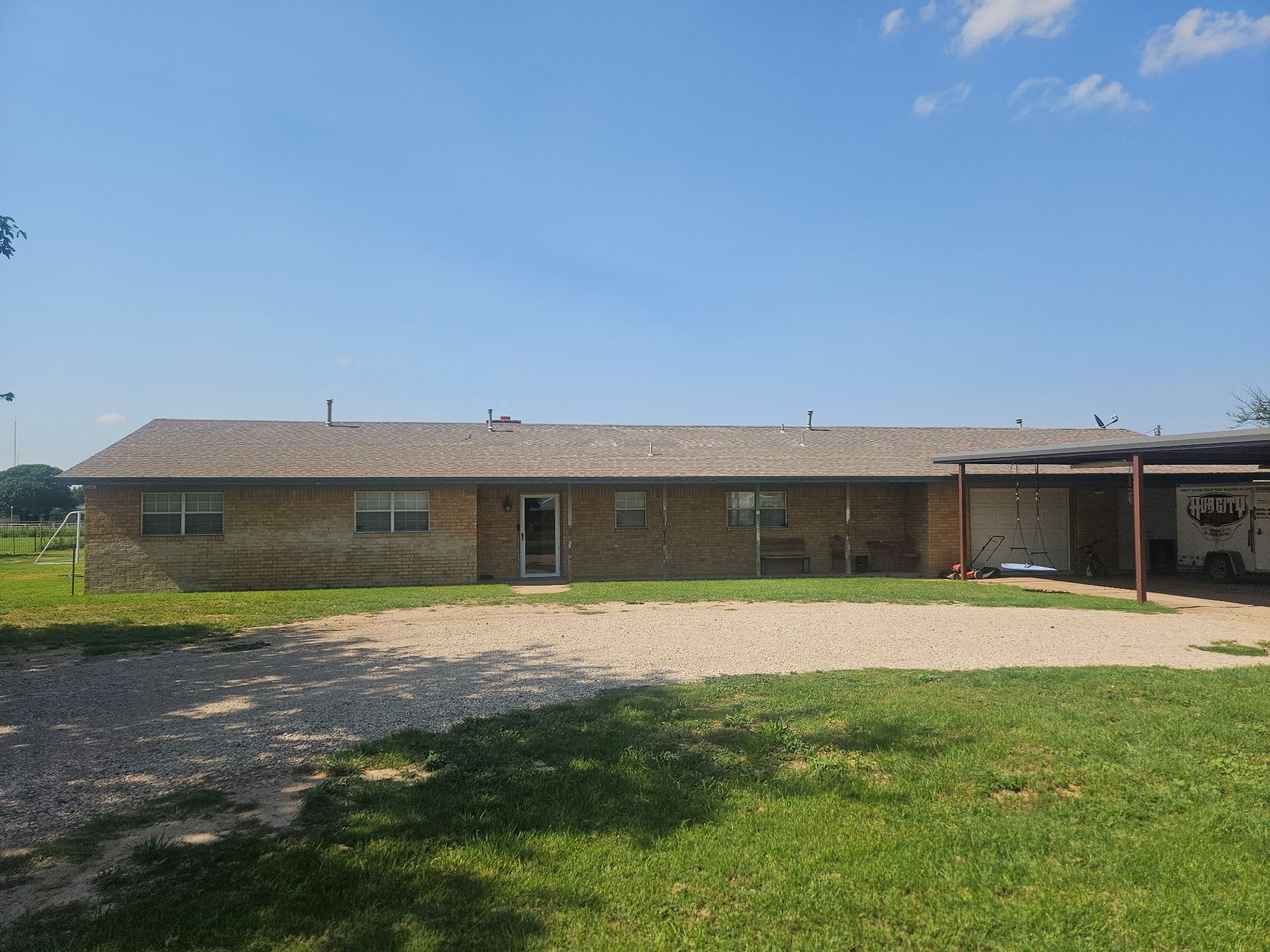Long, low brick building with gravel driveway and carport on a sunny day.