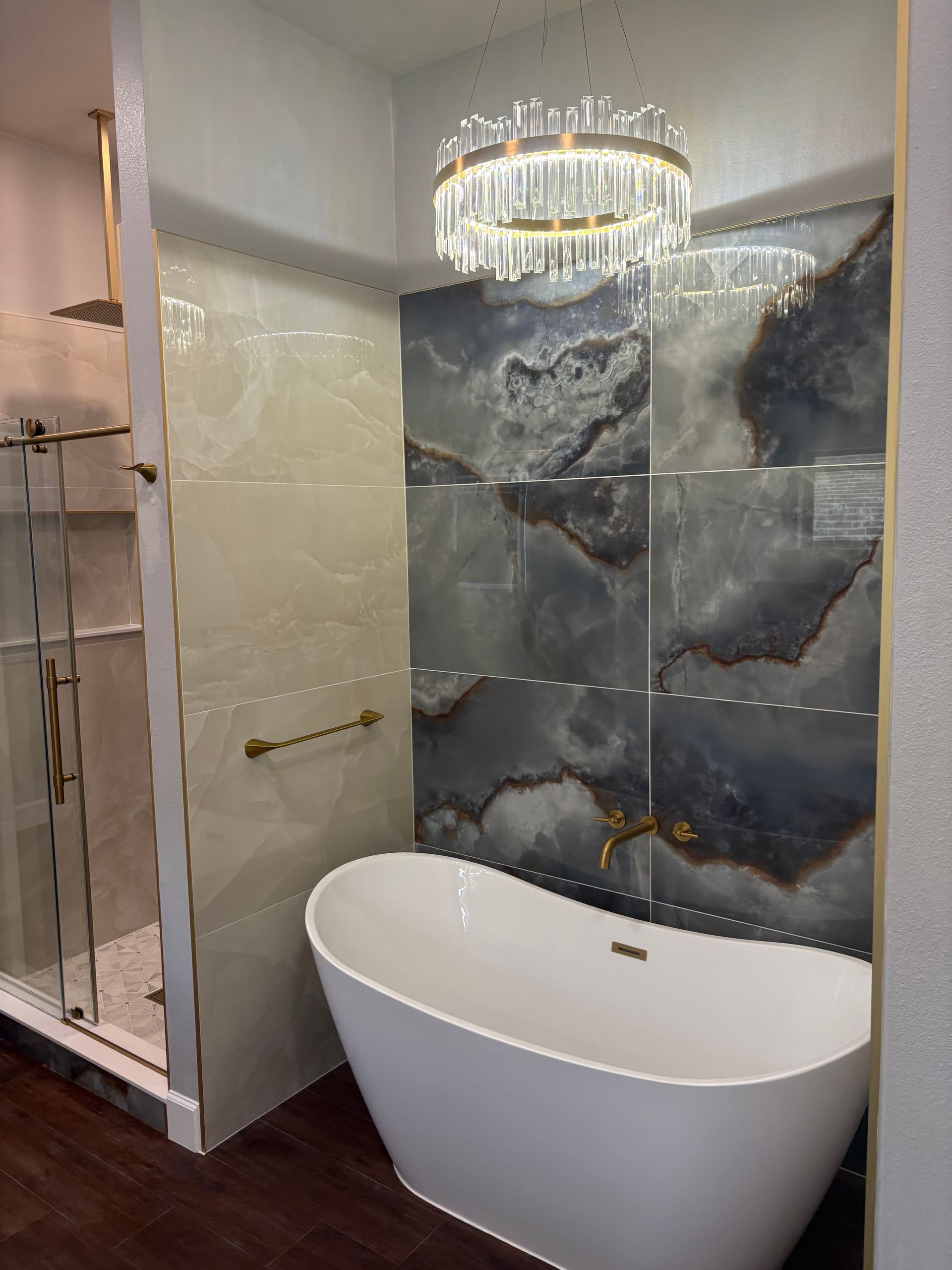 Bathroom with a white tub, blue and beige wall tile, glass shower, and gold fixtures.