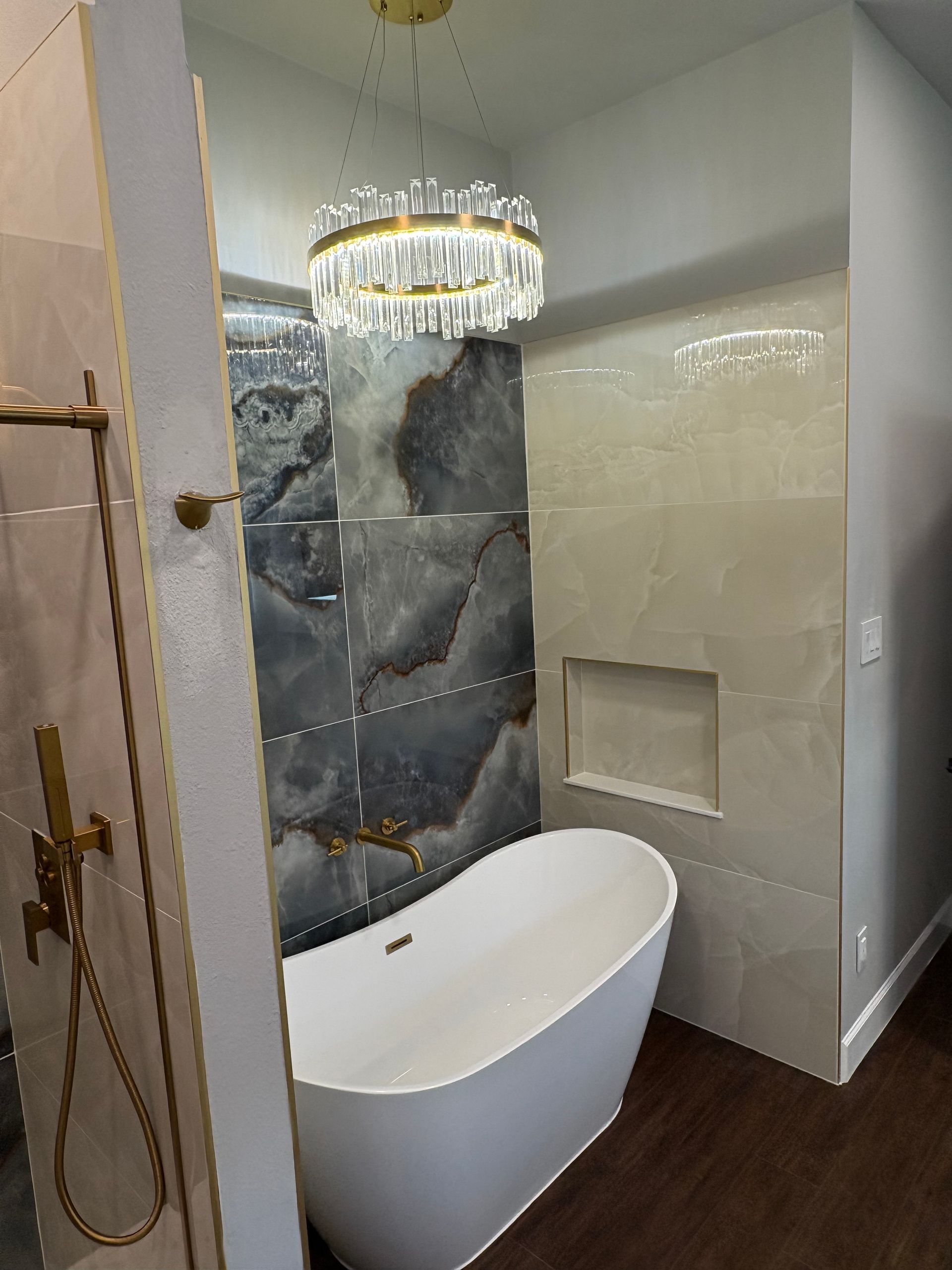 Luxurious bathroom with a white tub, chandelier, and marble-like tile.