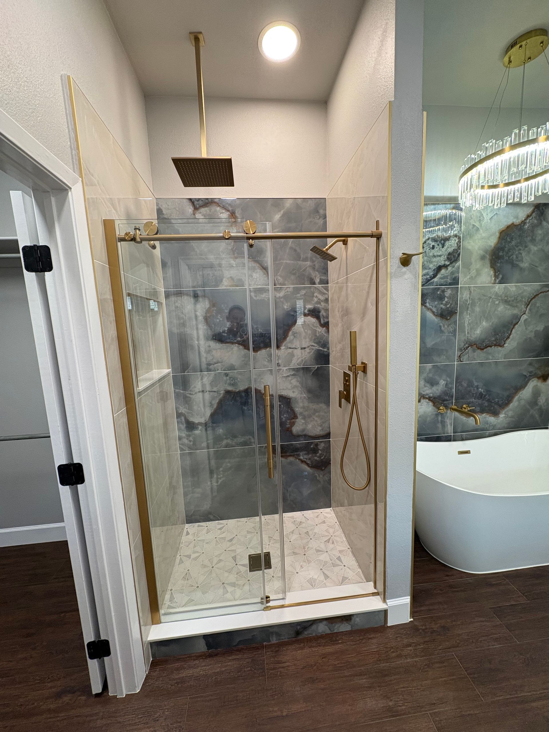 Bathroom with gold shower fixtures and glass doors; marble tile walls and floor.