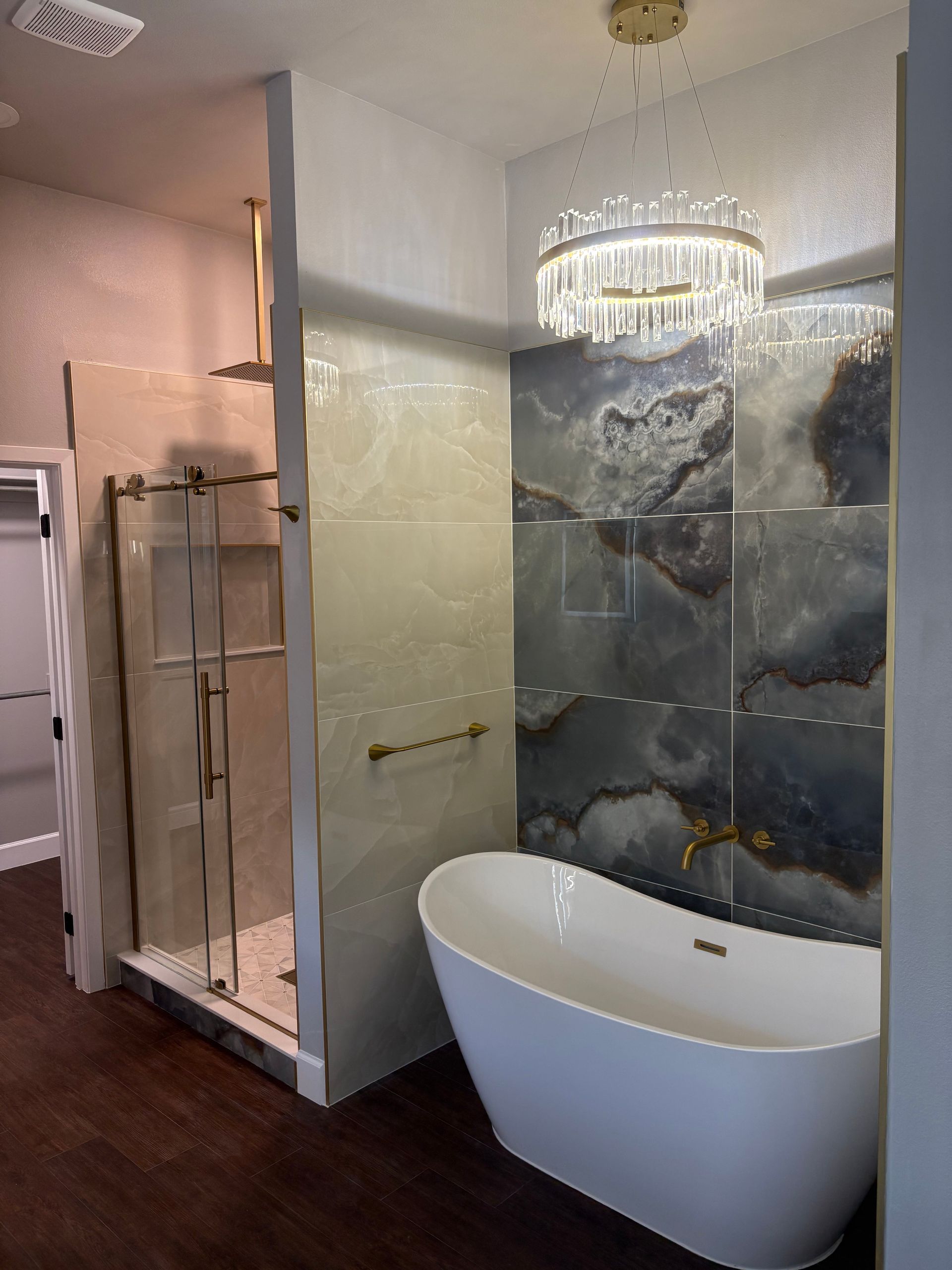 Luxurious bathroom with a standalone tub and a glass-enclosed shower, featuring gold fixtures and a decorative chandelier.