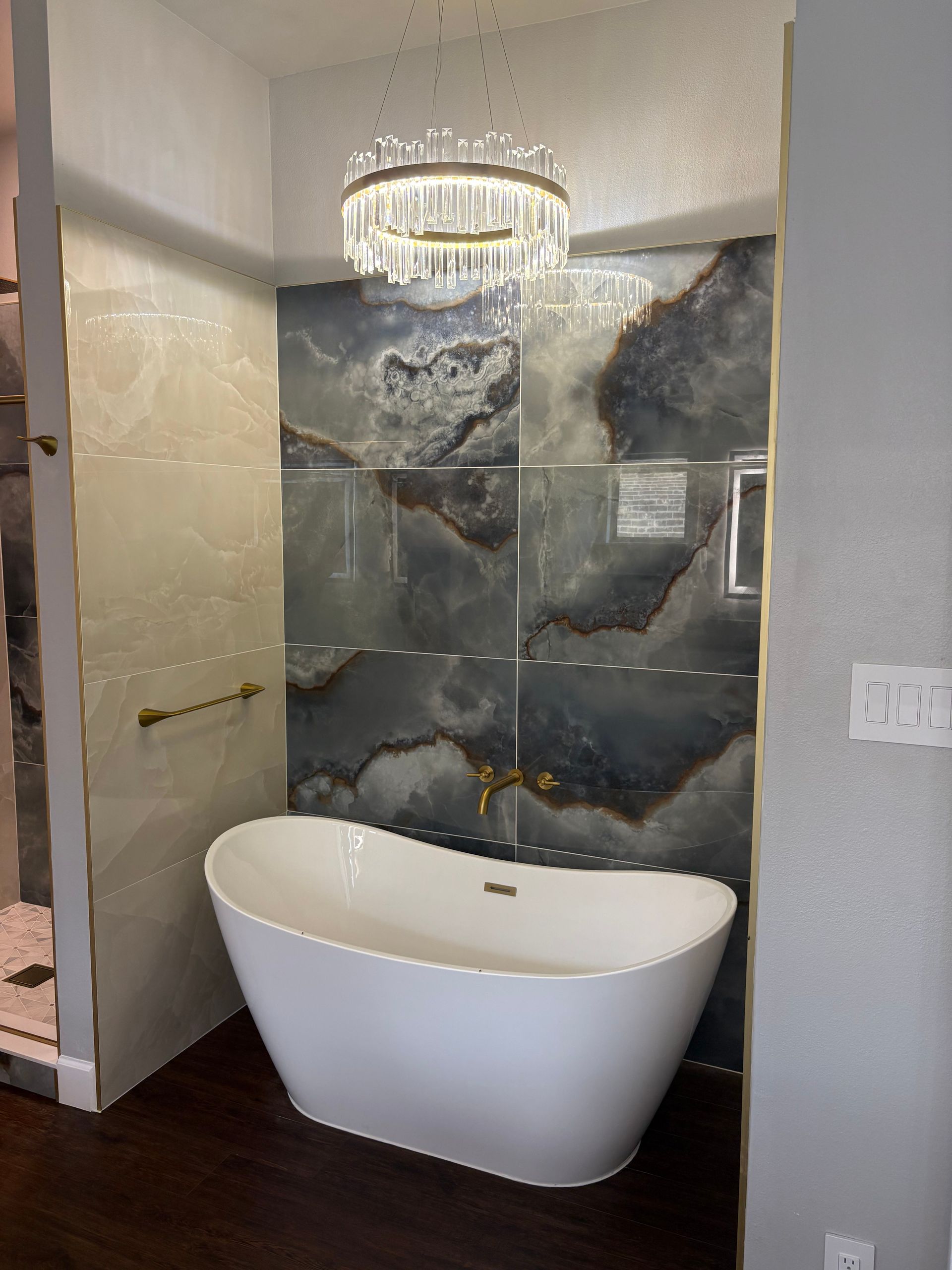 Modern bathroom with white freestanding tub, blue and cream tile walls, and a crystal chandelier.