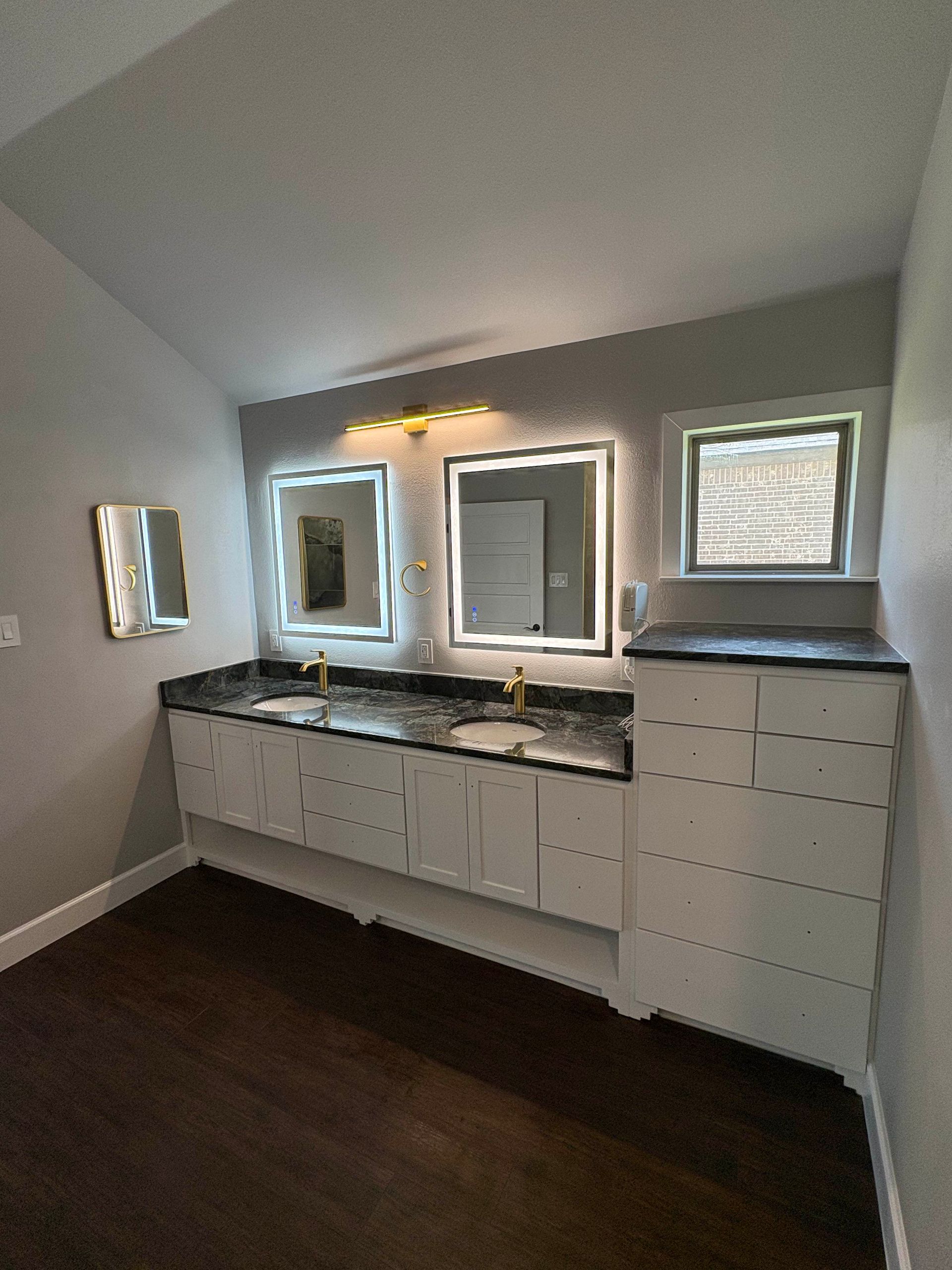 Bathroom with floating white vanity, black countertop, gold fixtures, and lit mirrors.