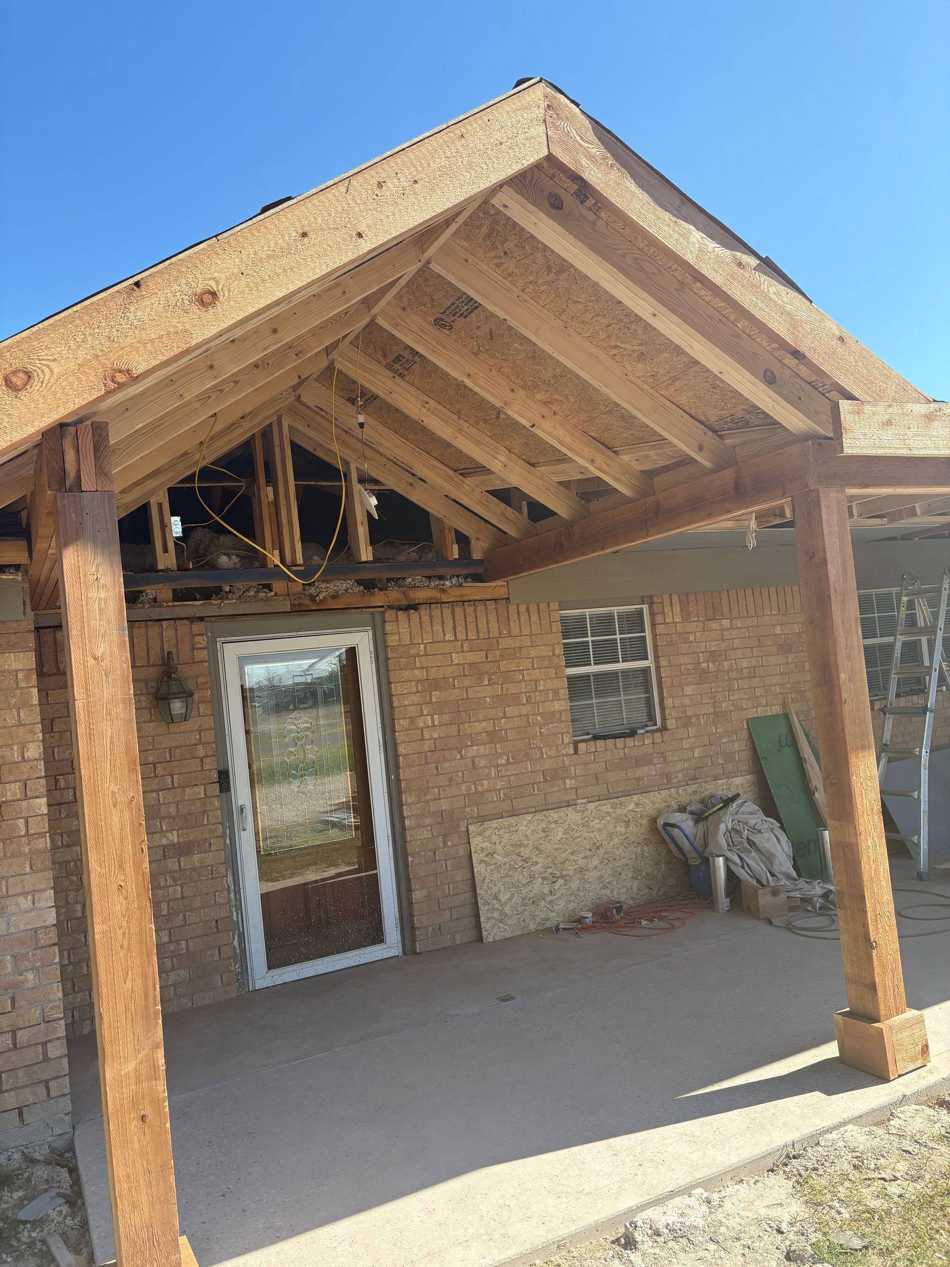 A partially constructed porch with wooden beams, attached to a brick home.