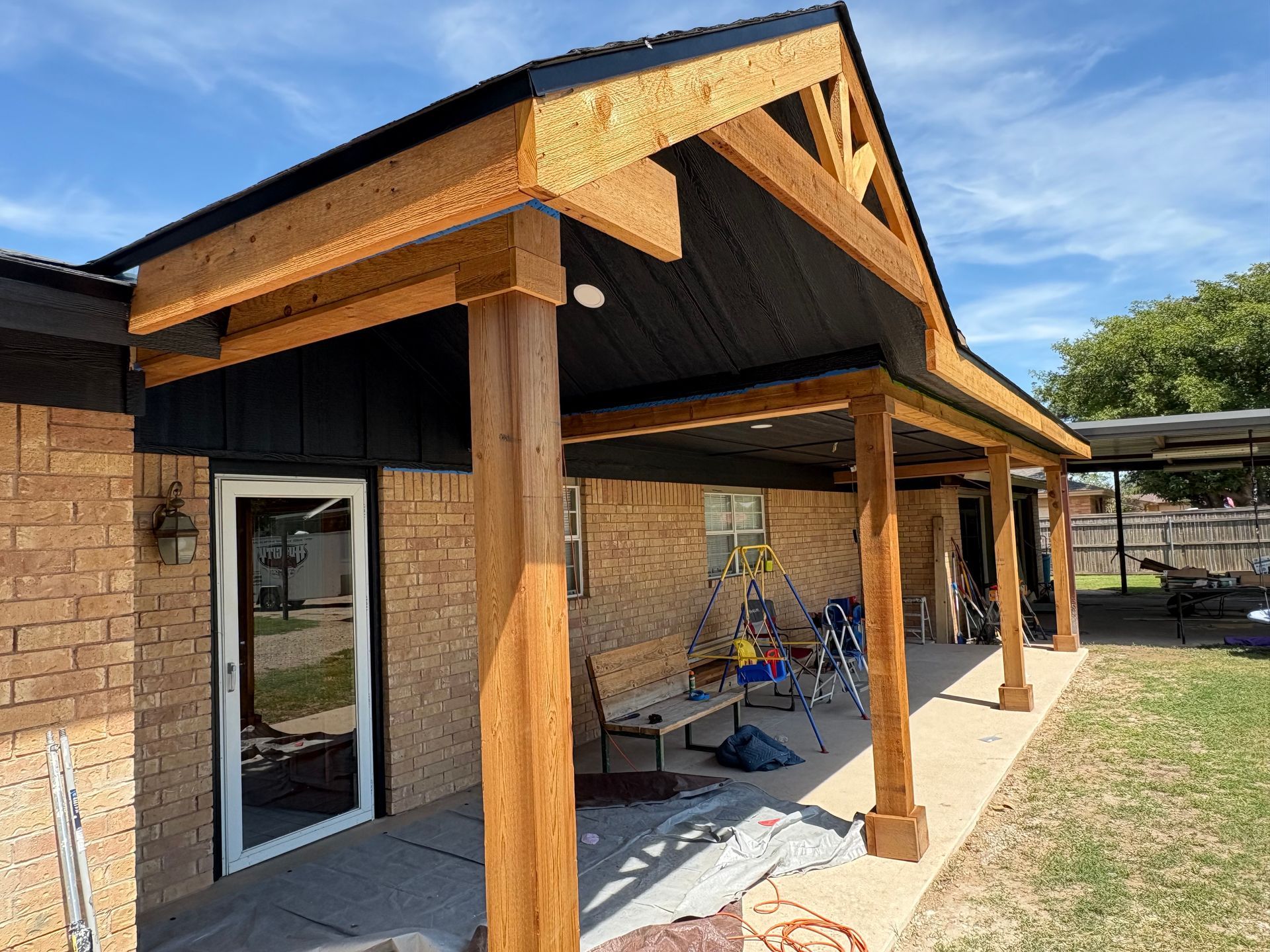 Covered wooden patio attached to a brick house on a sunny day.