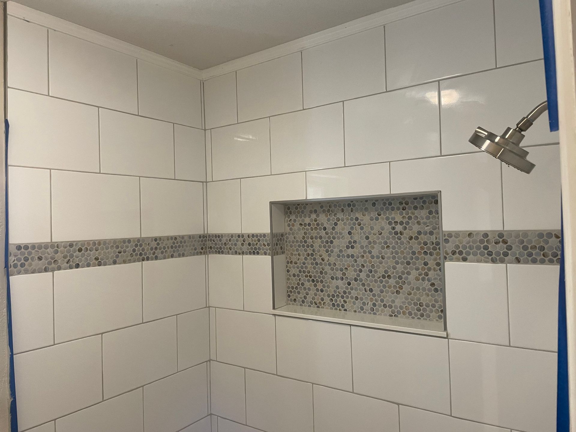 Tiled shower stall with a mosaic tile niche. White tiles with a grey mosaic accent band. Showerhead visible.