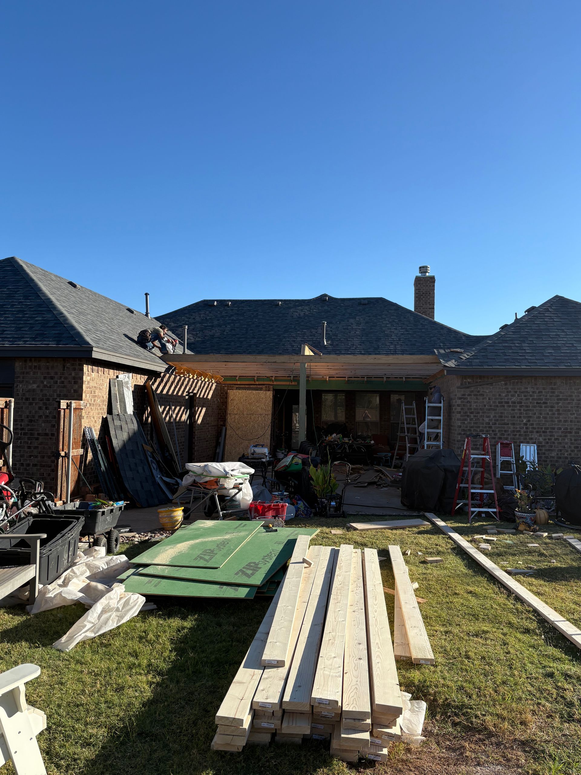 Backyard construction site; boards on the ground, cluttered with debris, house in background, clear blue sky.