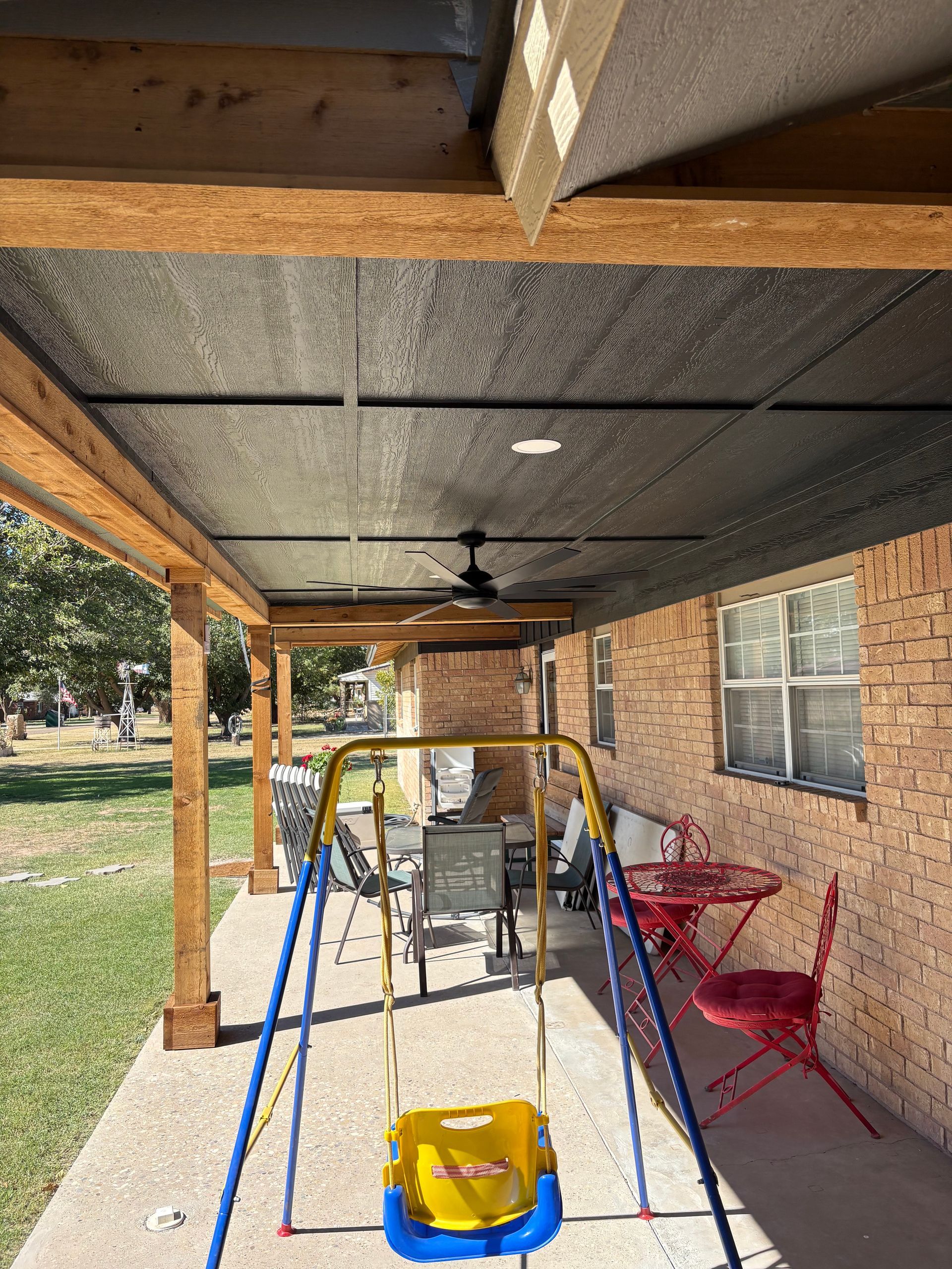 Outdoor patio with a swing set, table, and ceiling fan under a shaded roof.