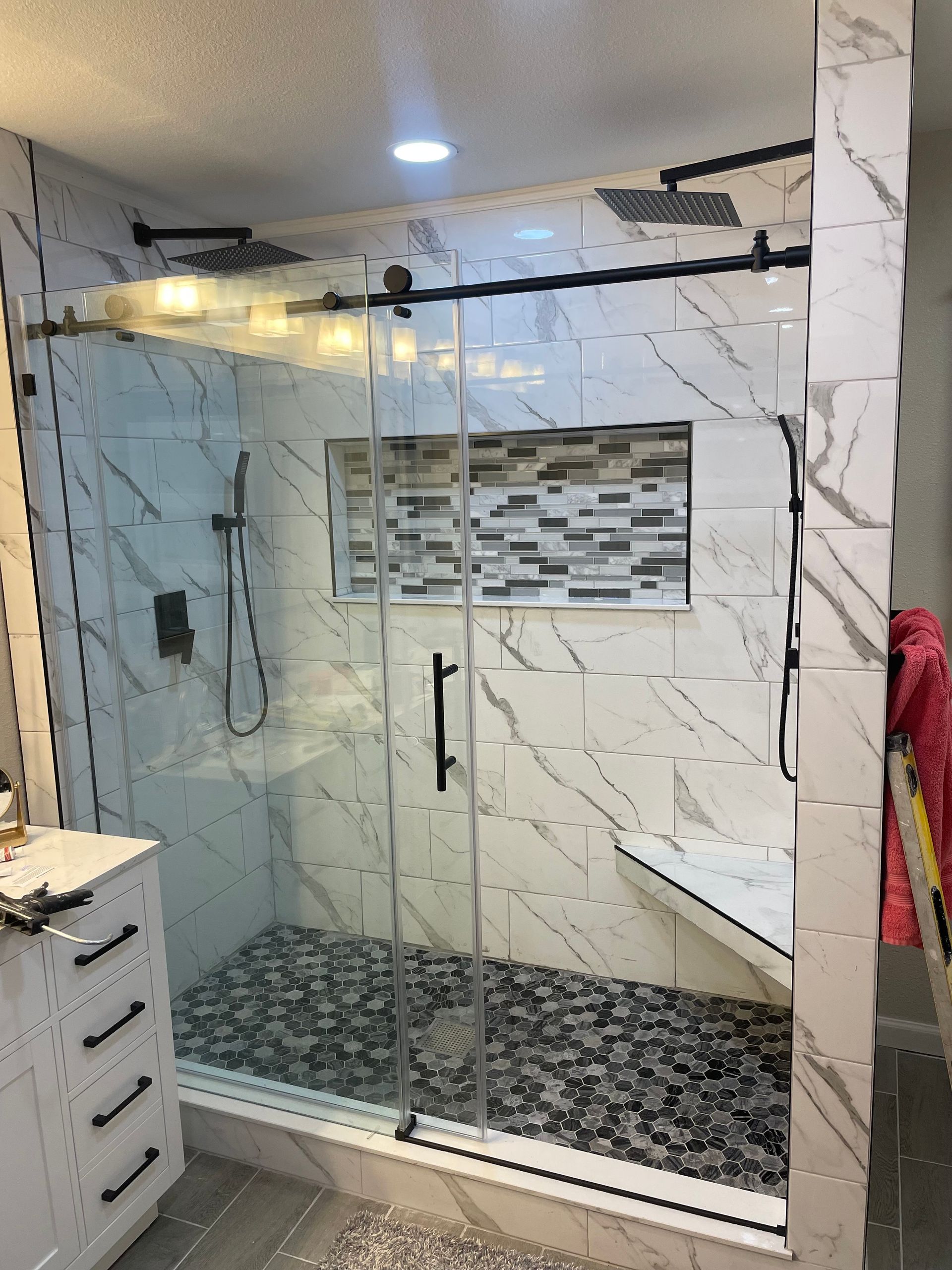 Modern shower with marble-look tile, glass doors, pebble floor, and a built-in bench.