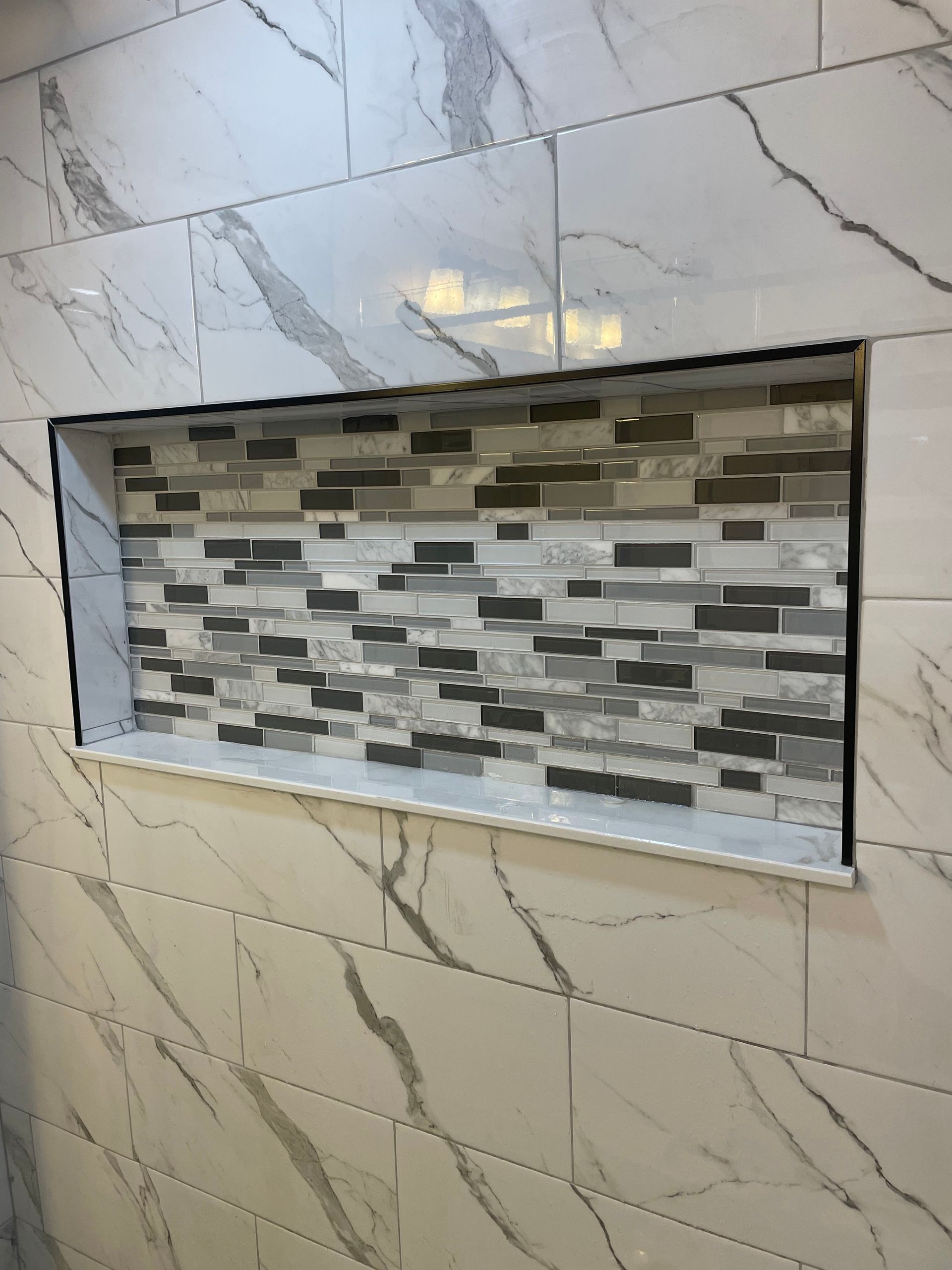 Shower niche with mosaic tile inside, framed by large, marbled wall tiles.