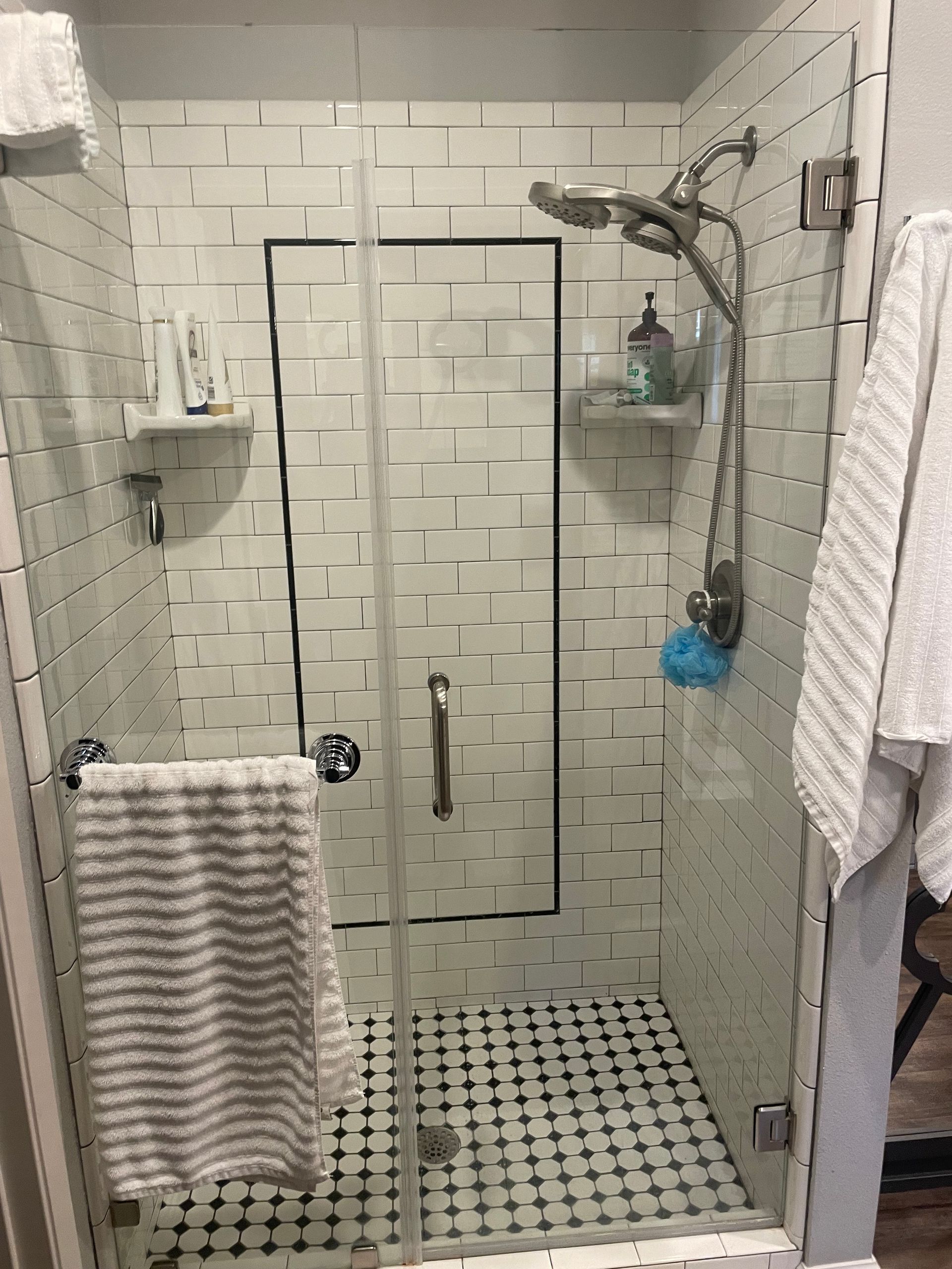 Shower stall with white brick tile, glass door, and black and white floor tiles.