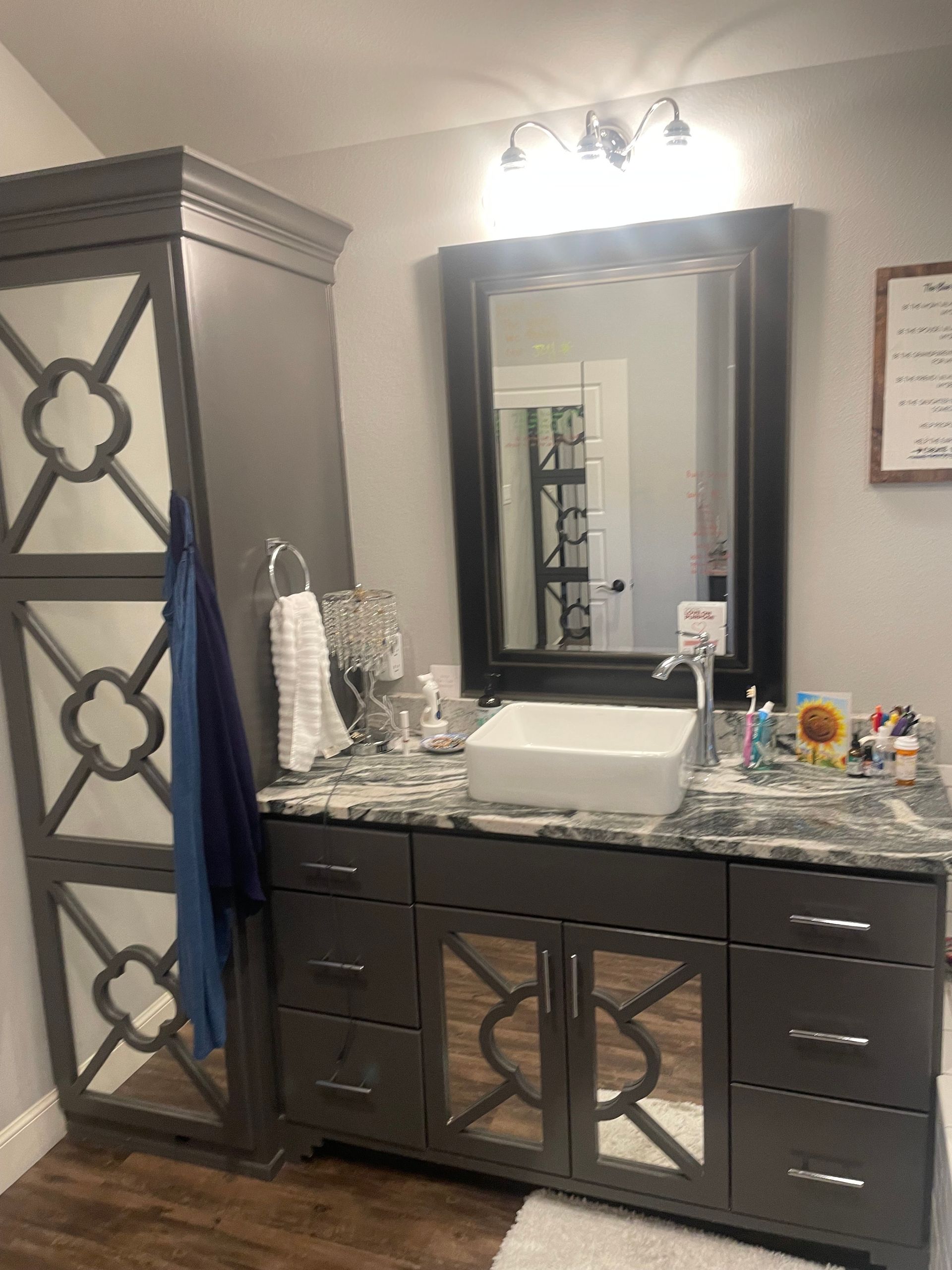 Bathroom with gray cabinets, large mirror, and a tall storage unit.
