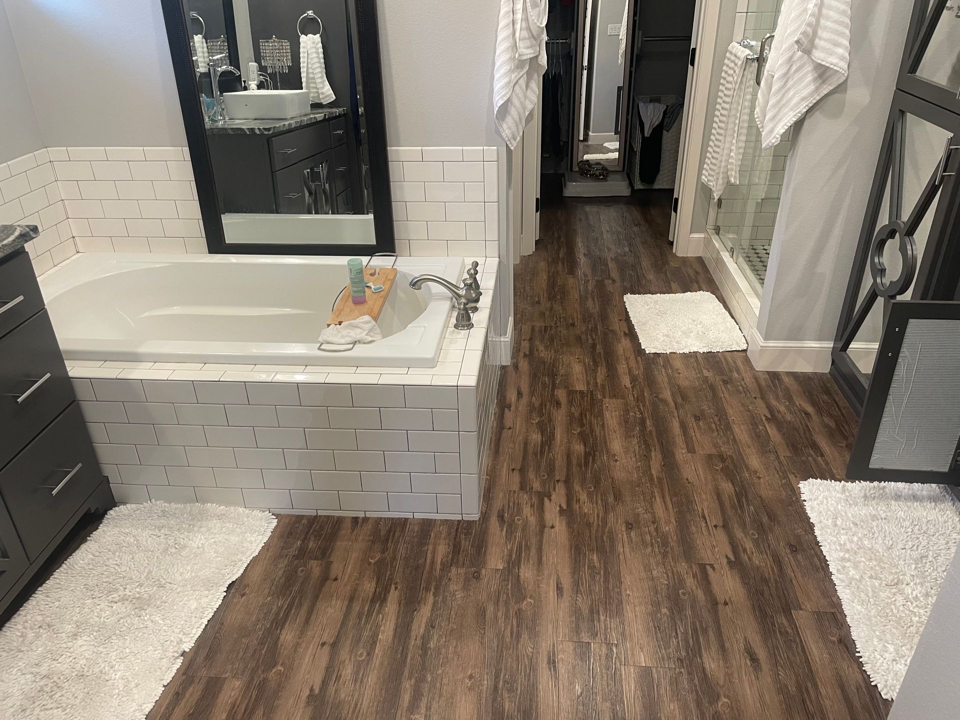 Bathroom with dark wood-look floor, white tile tub surround, and a mirror over the vanity.