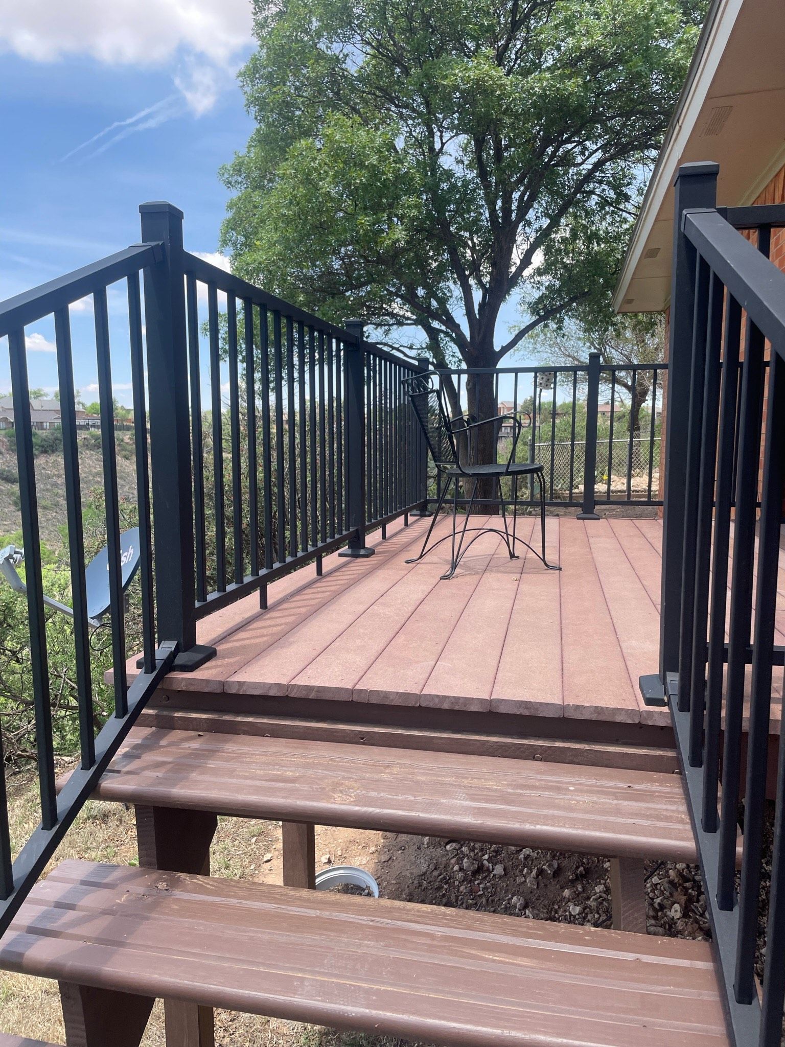 Wooden deck with stairs, black railing, and view of trees and sky.