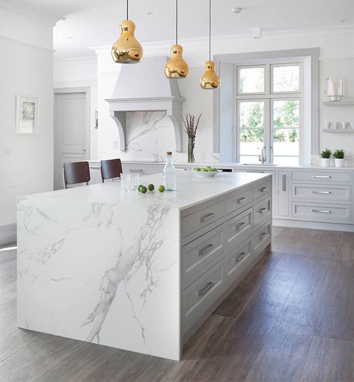 Bright kitchen with white marble island, grey cabinets, gold pendant lights, and wooden floors.