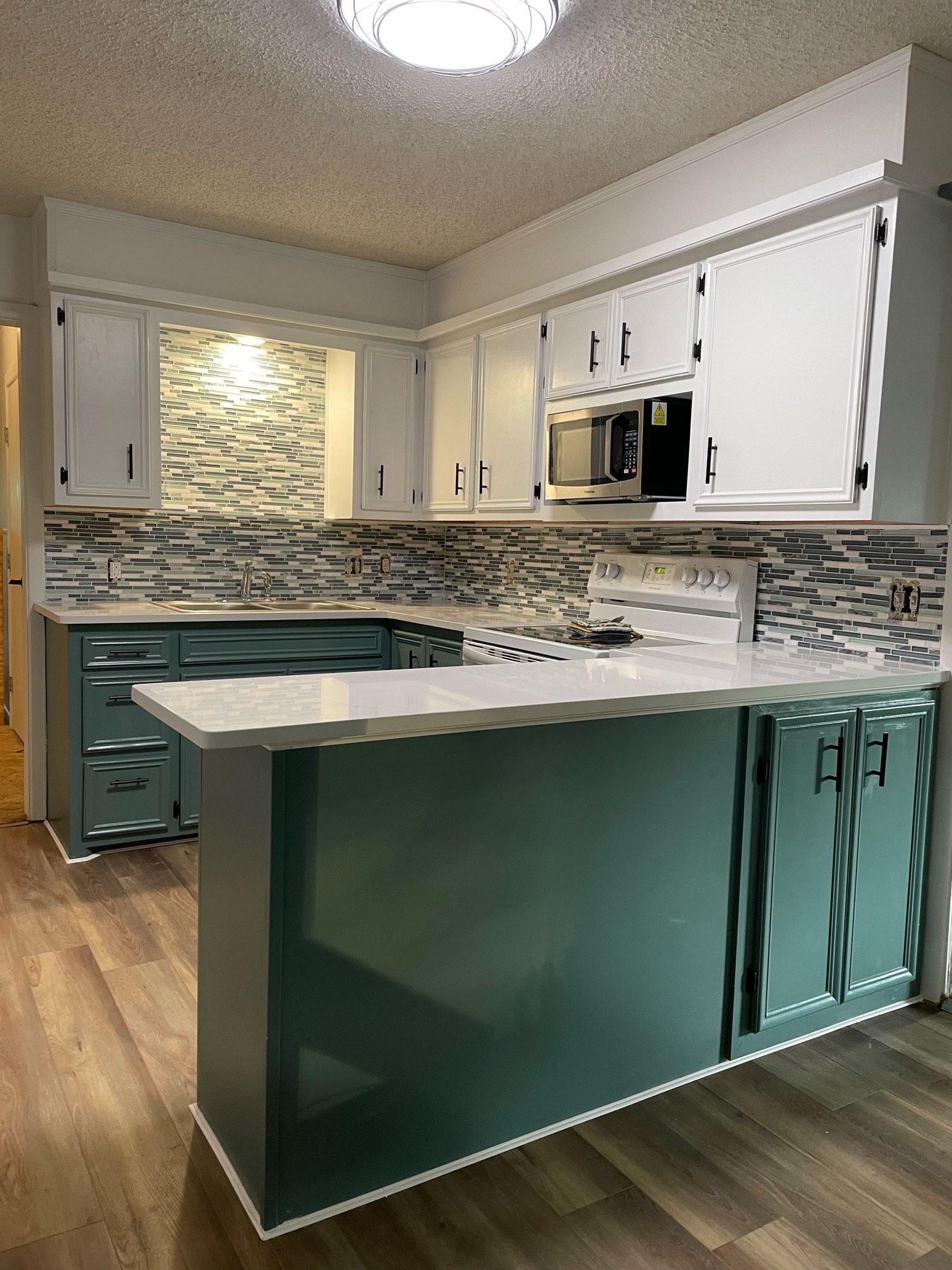 Kitchen with teal island, white cabinets, and gray backsplash.