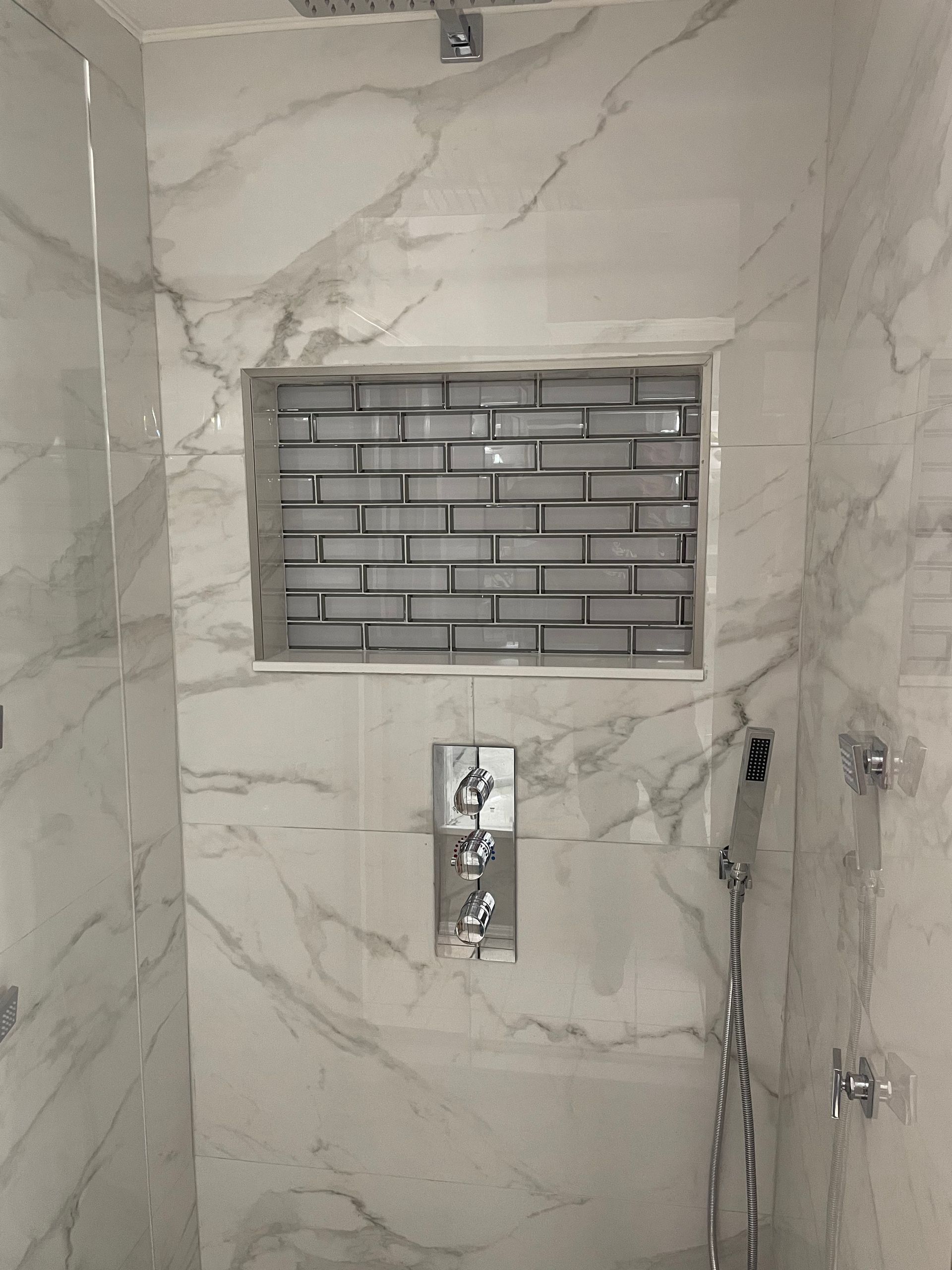Shower with white marble-patterned tile, a gray brick-tiled niche, and silver fixtures.