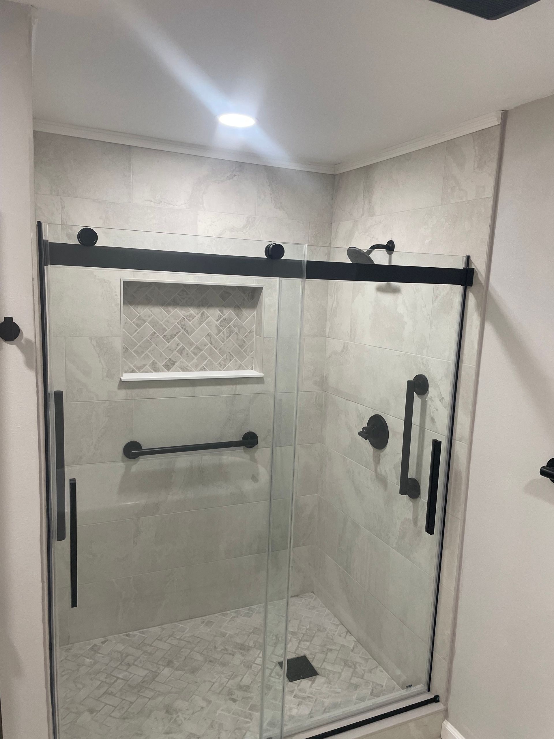 Modern shower with glass doors, black hardware, gray tile, and a built-in shelf.