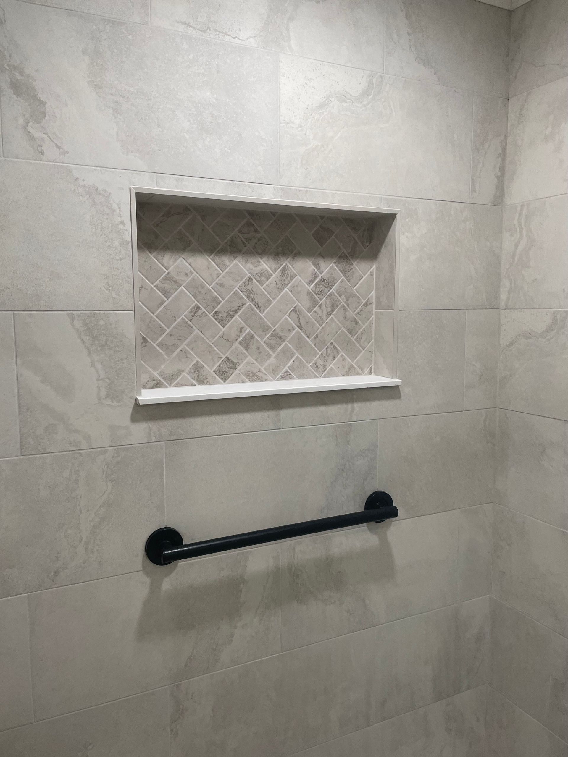 Tiled shower with built-in shelf and black towel bar. Gray tiles with a mosaic backsplash in shelf.