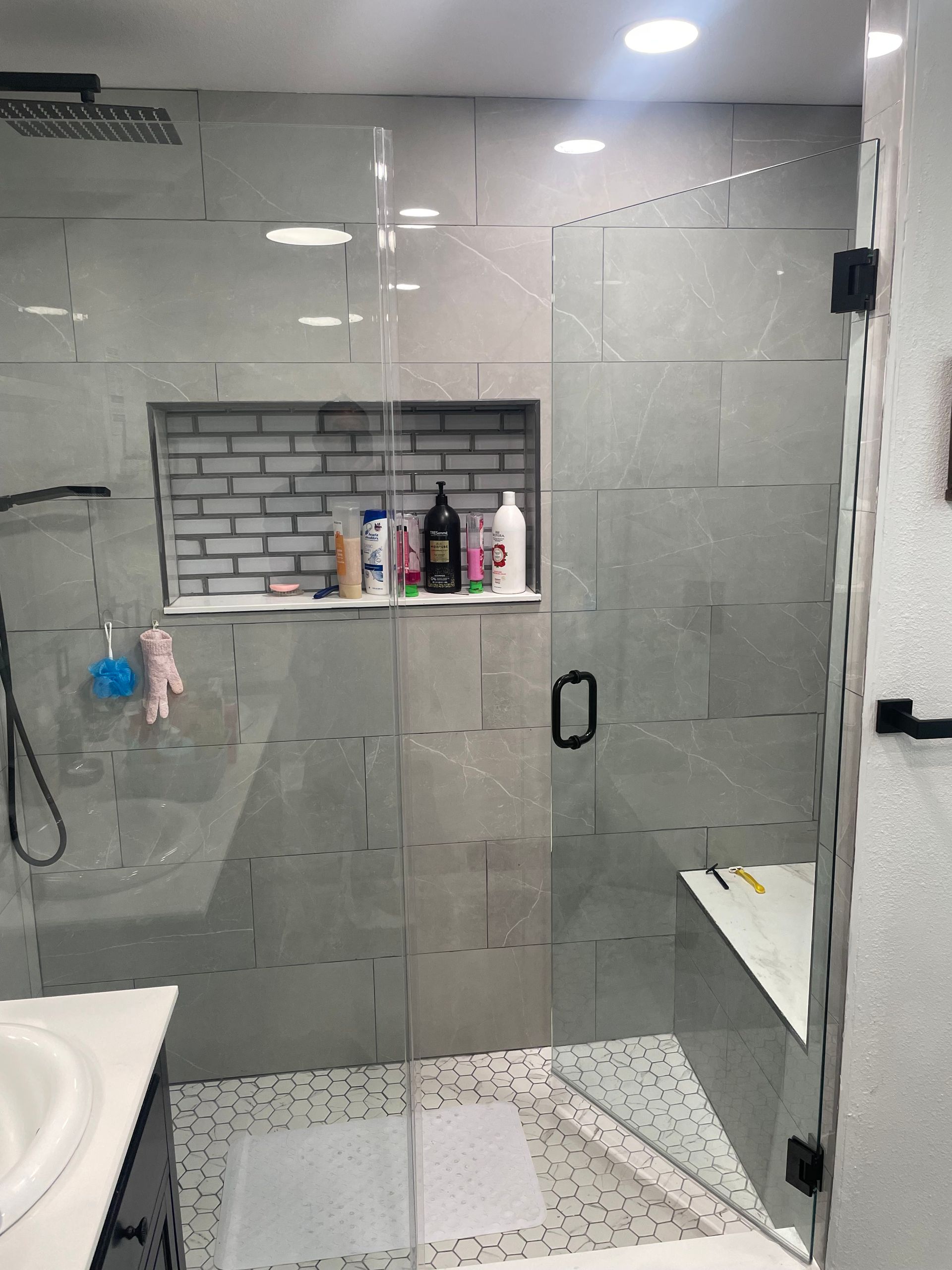 Modern bathroom with glass shower enclosure, gray tile walls, built-in shelf, black hardware.